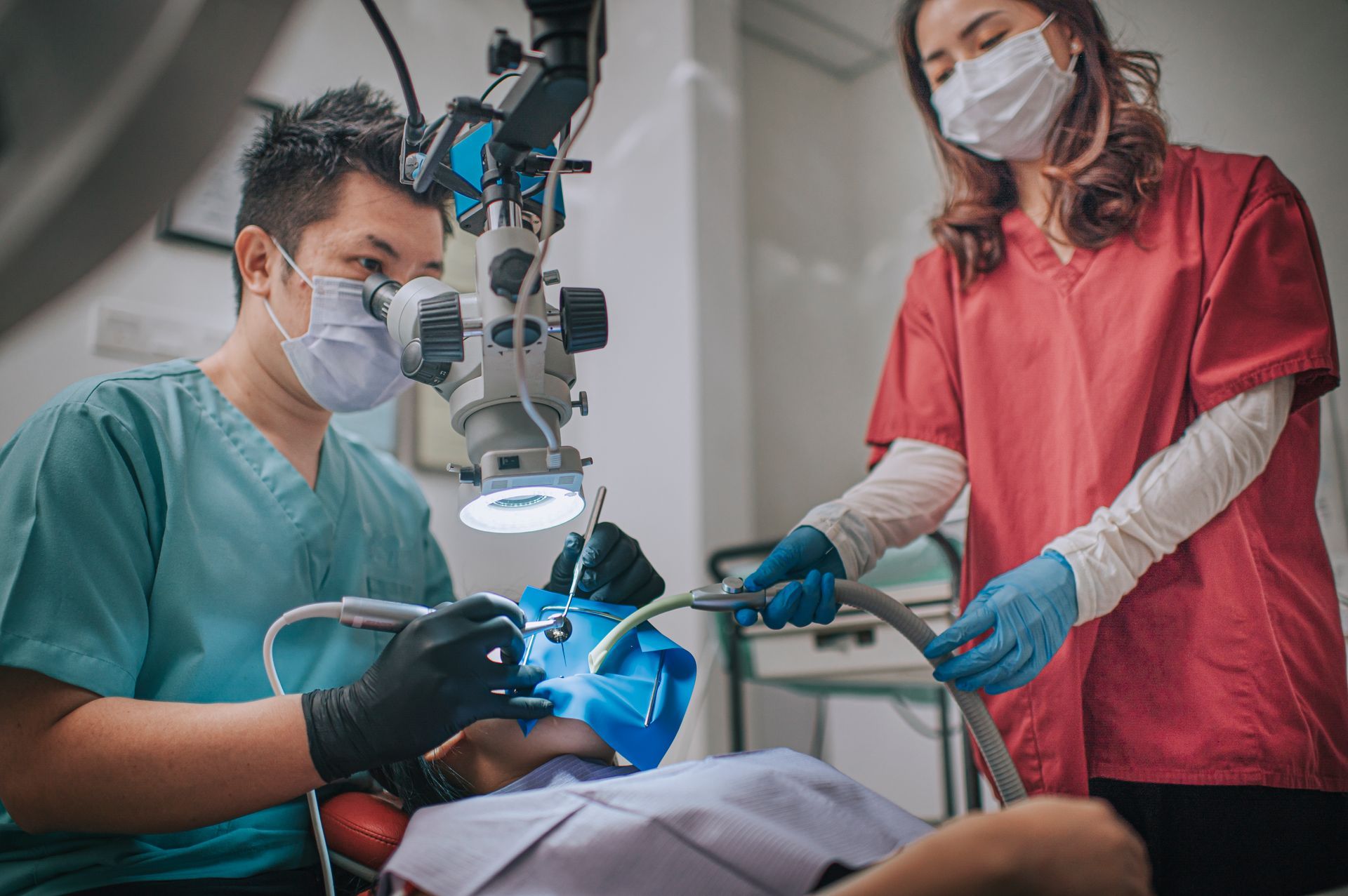 A dentist and a nurse are working on a patient 's teeth under a microscope.
