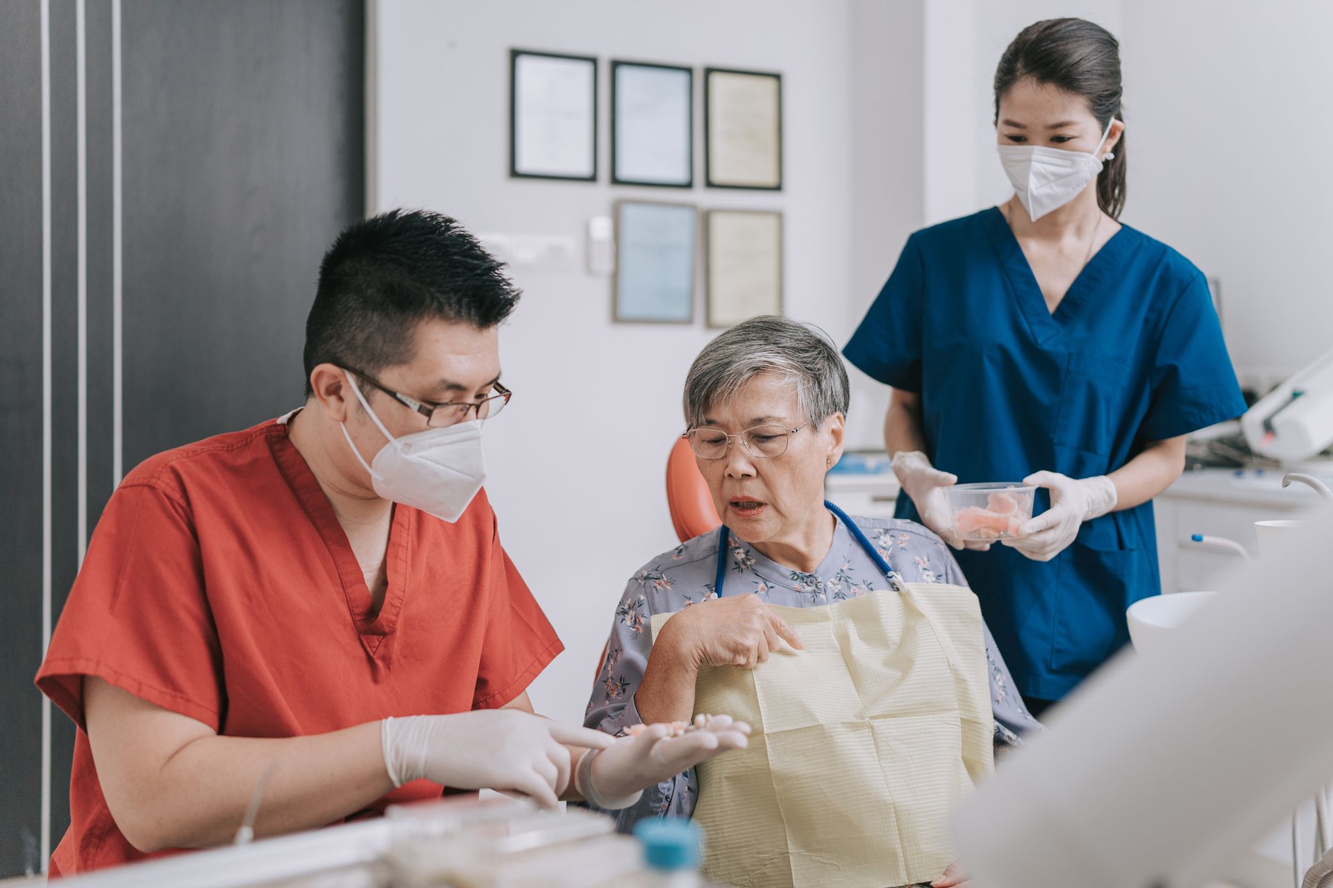 A dentist is talking to an elderly woman in a dental chair.