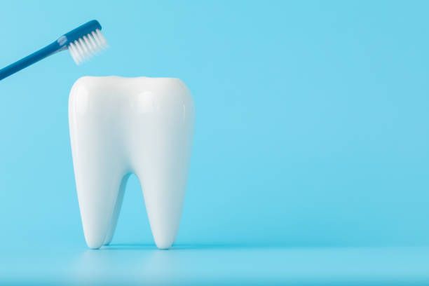A white tooth with a blue toothbrush on a blue background.