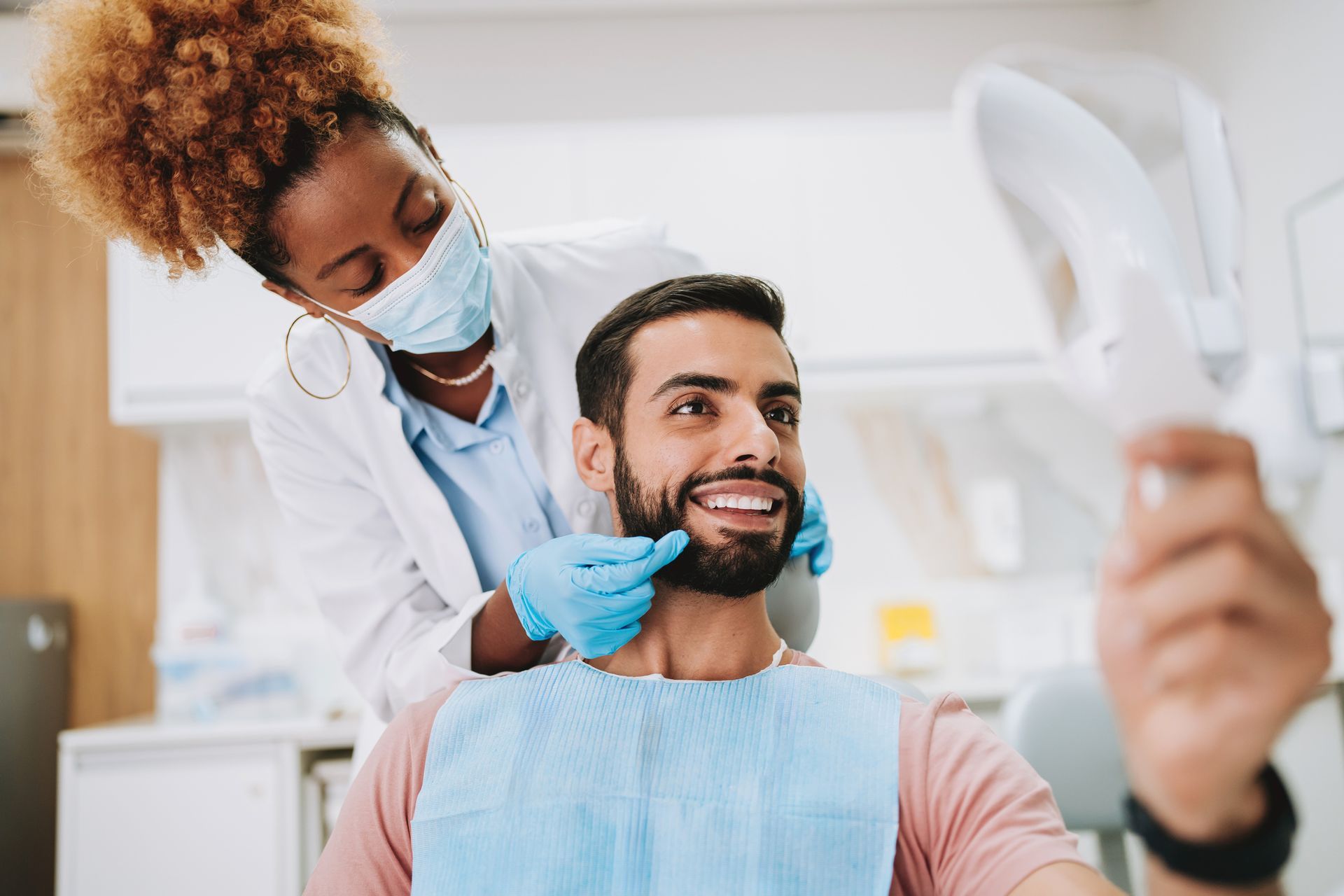 A man is taking a selfie at the dentist while the dentist examines his teeth.