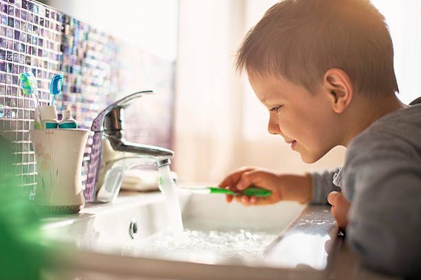 A young boy is brushing his teeth in a sink.