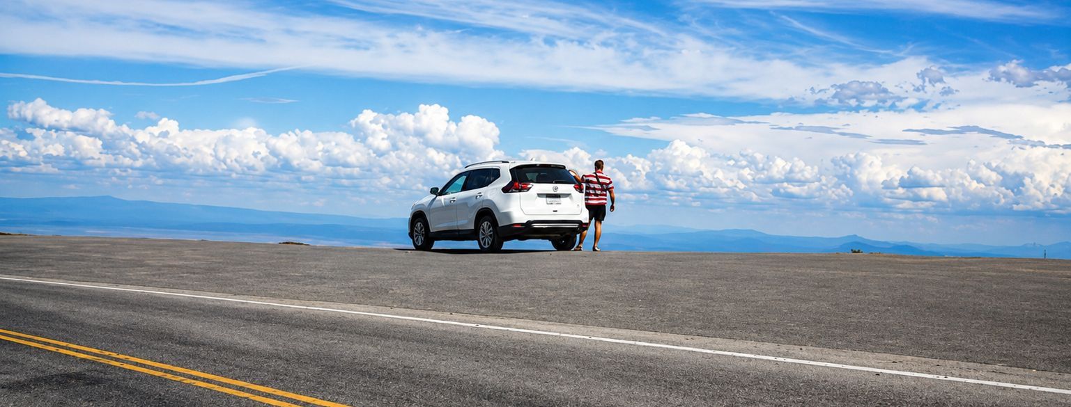 SUV parked on a wide road with a person standing beside it under a blue sky