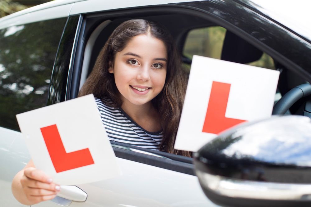 A Girl Is Sitting In A Car Holding Two Learning Plates — Darran Thompson Driver Training in Wollongong, NSW