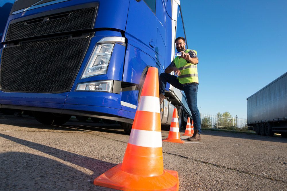A Man Is Standing Next To A Blue Semi Truck And Showing His License — Darran Thompson Driver Training in Wollongong, NSW
