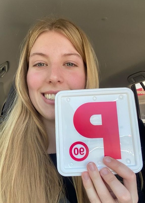 A Woman In A Car Is Holding A License Plate With The Letter P On It — Darran Thompson Driver Training in Wollongong, NSW