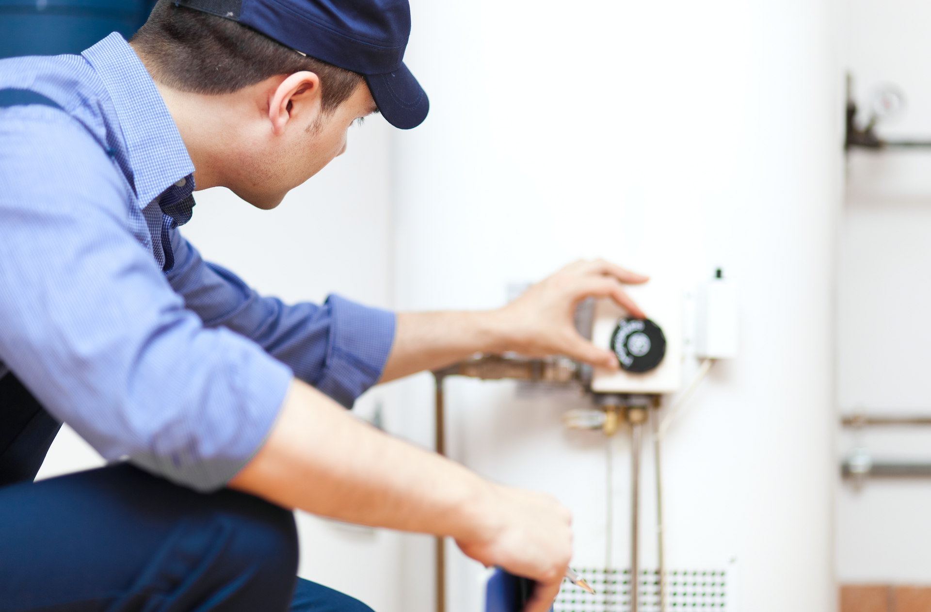 A man is kneeling down fixing a water heater.