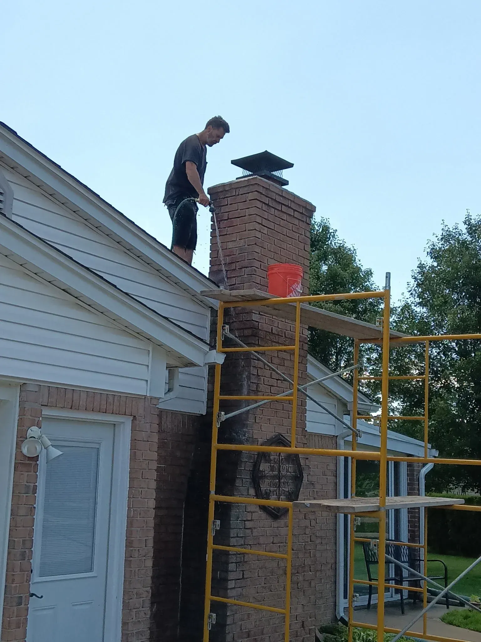 Worker on yellow scaffold repairing a brick chimney on a house roof