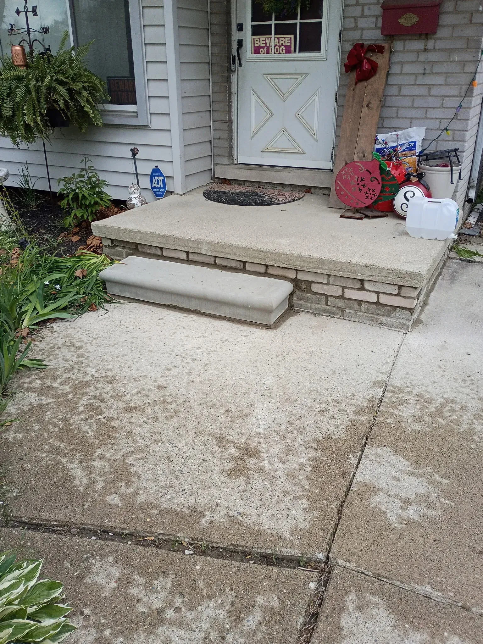 Front porch with concrete steps, a gray door, and potted plants beside a light-colored house.