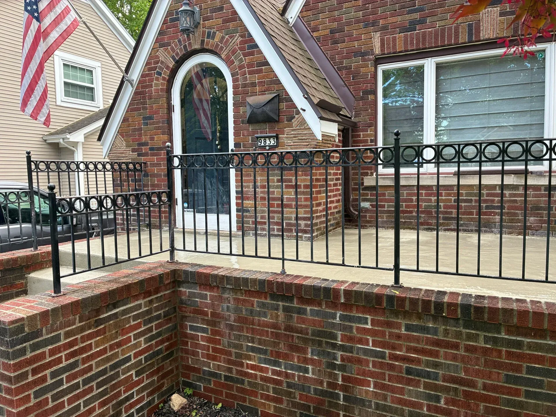 Brick townhouse entrance with black metal railings, arched door, and American flag beside a window.