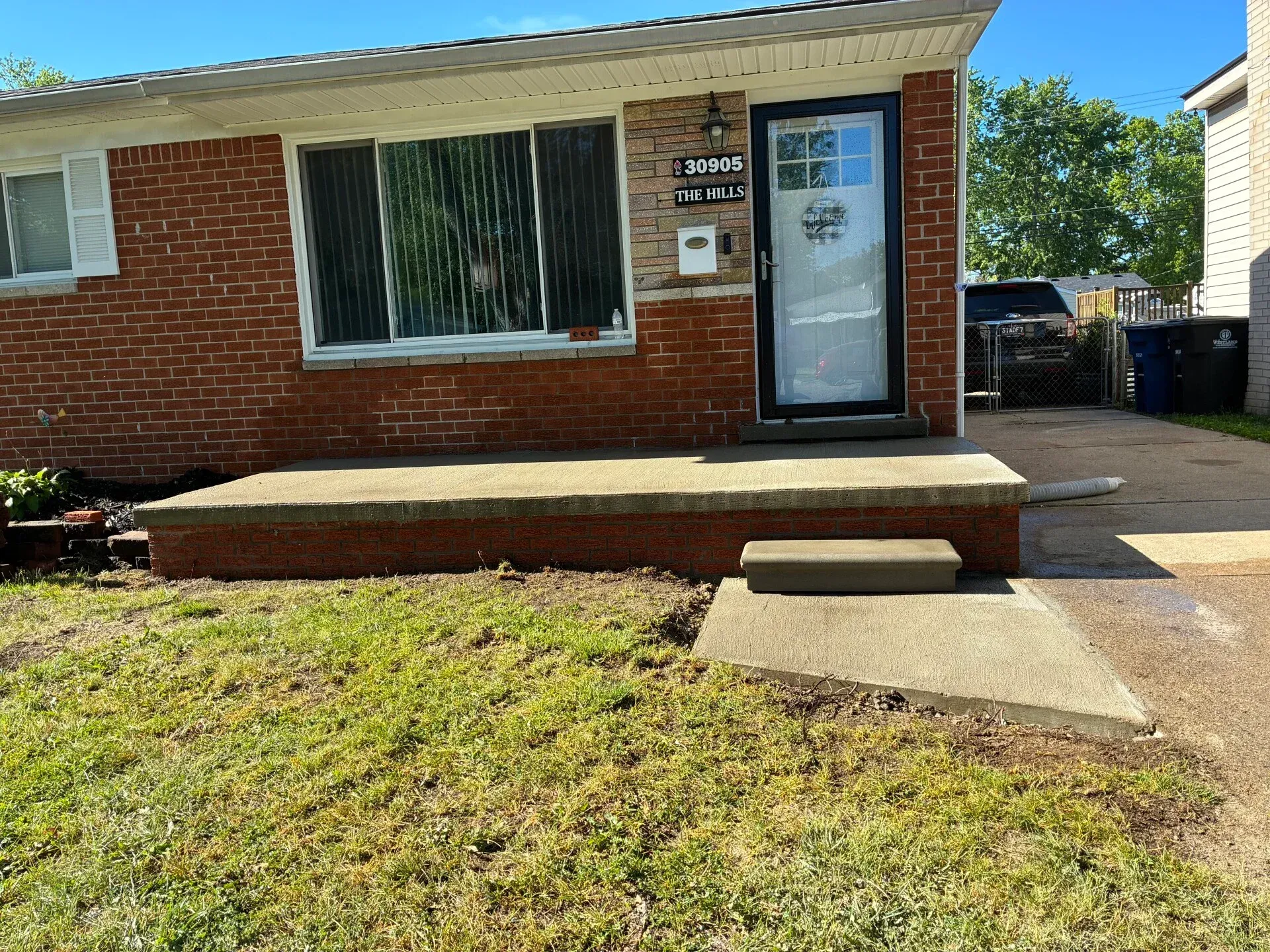 Brick house front entrance with concrete steps and a walkway leading to the door