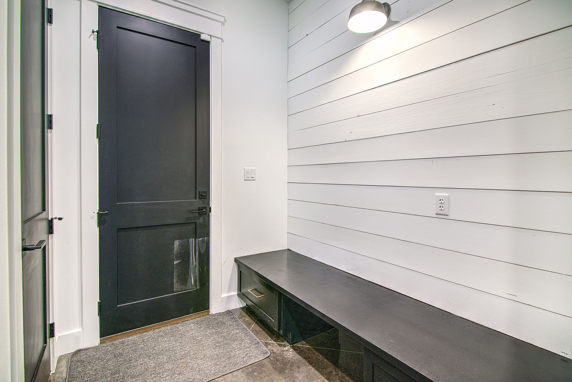 A hallway with a black door and a bench.