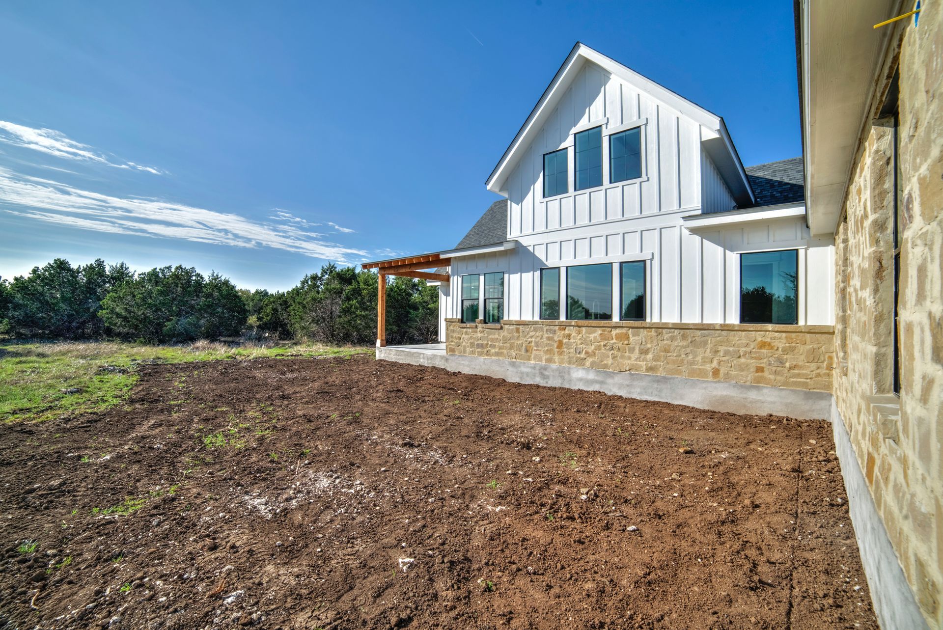 A white house with a lot of windows is sitting on top of a dirt field.