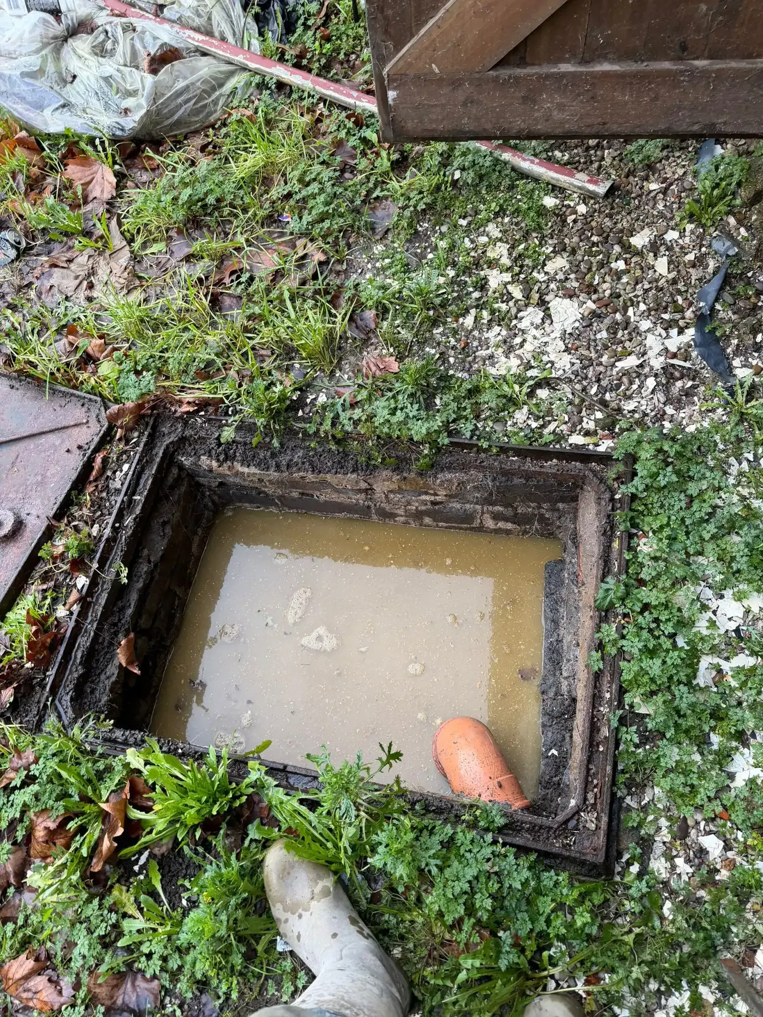 A metallic rain gutter with an icicle hanging from the end, set against a snow-covered wall.