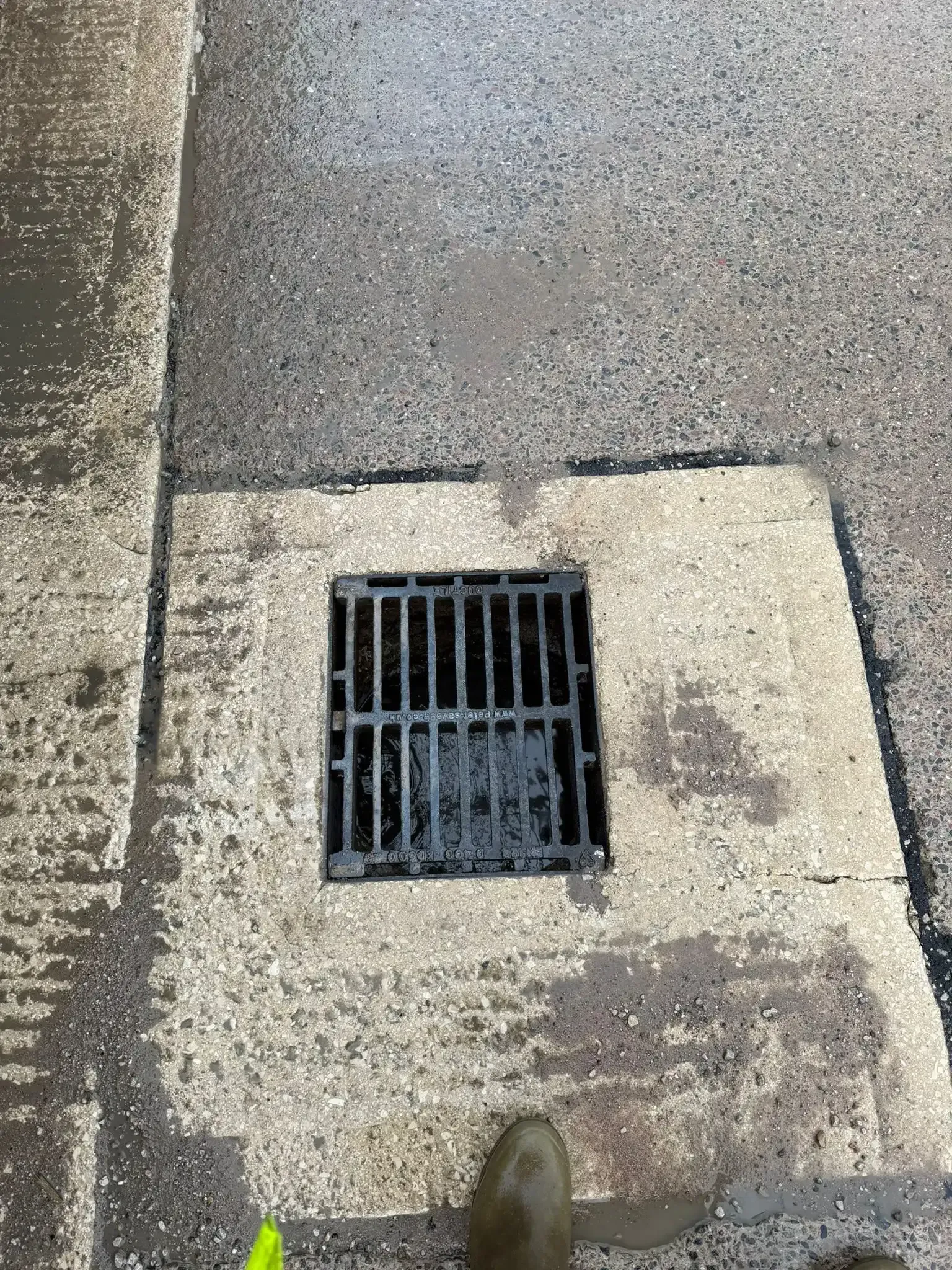 Workers in orange and blue coveralls and boots near an open manhole, using a hose from a truck.