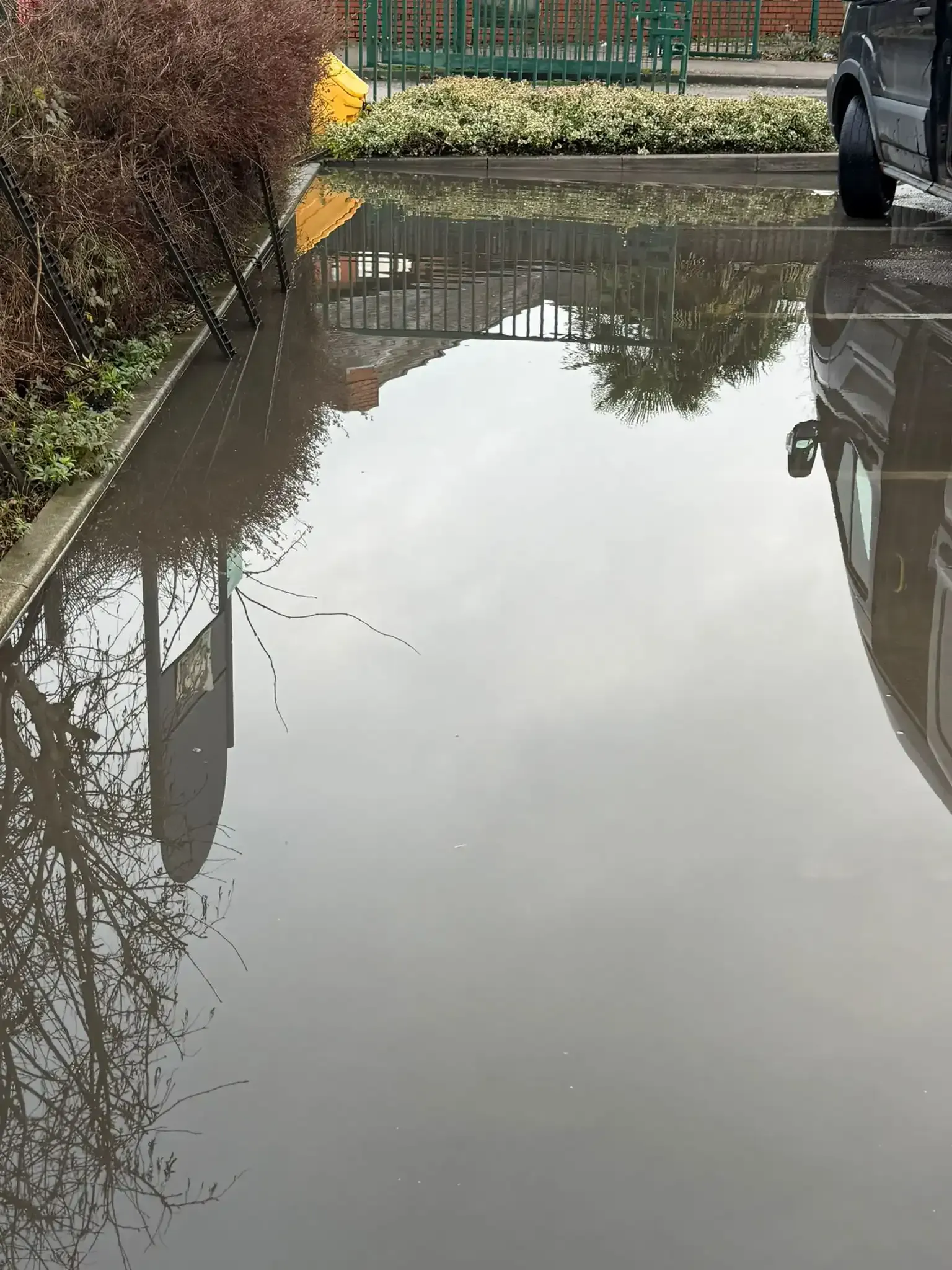 A metallic rain gutter with an icicle hanging from the end, set against a snow-covered wall.