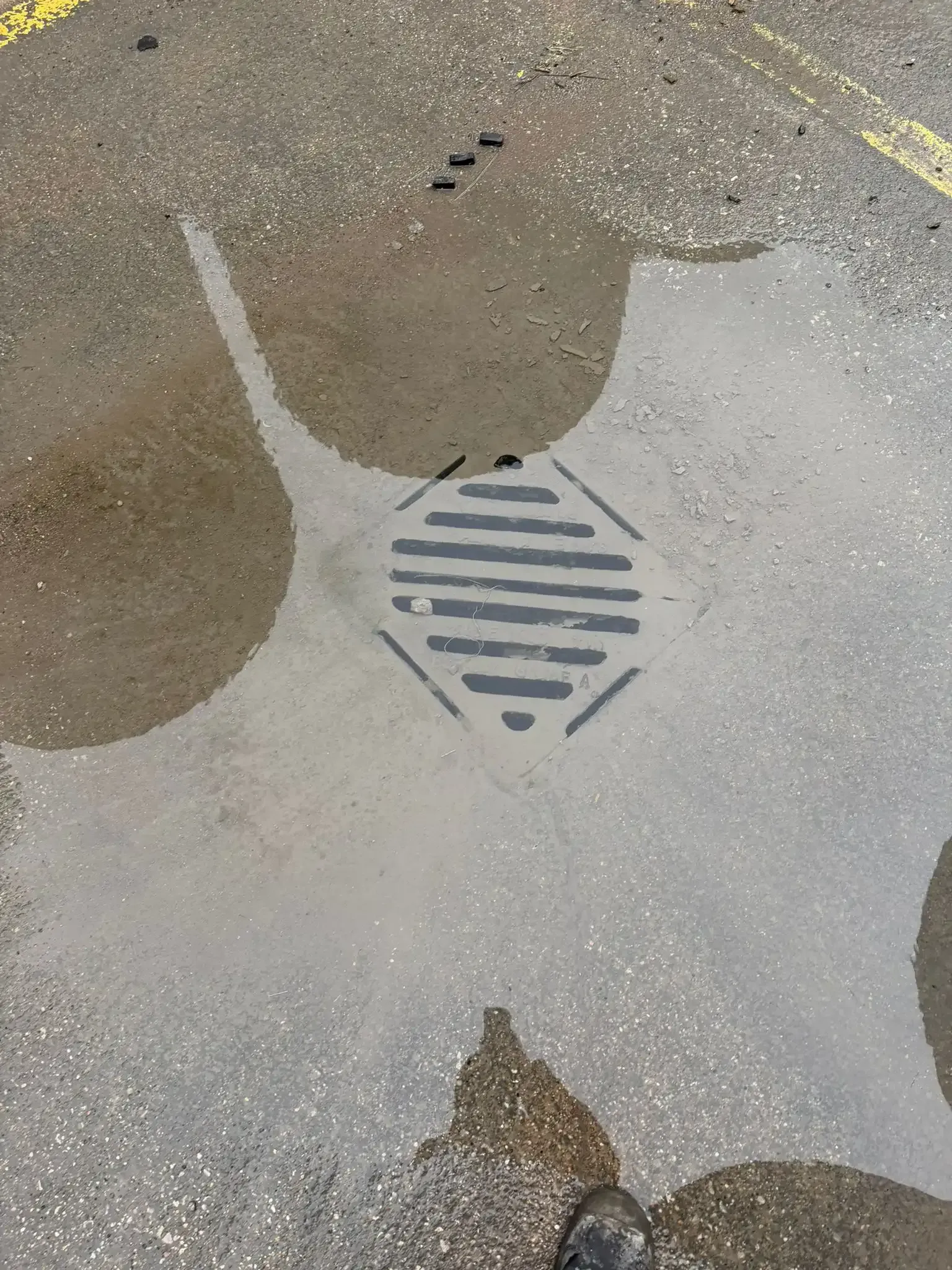 Icy water dripping from a metal downspout, creating a frozen column; snow on the ground.
