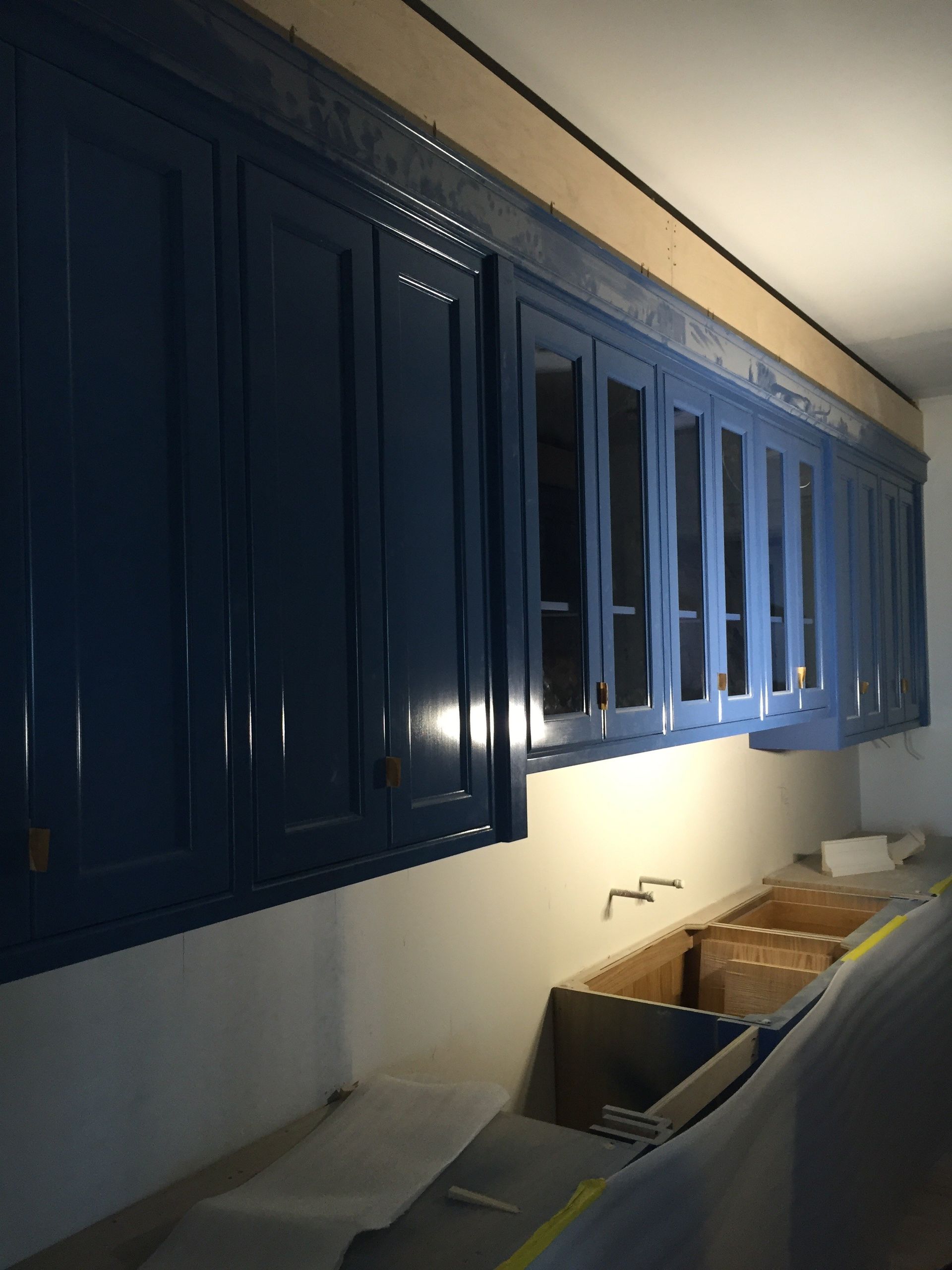 Blue kitchen cabinets with glass-fronted sections above a sink area under construction.