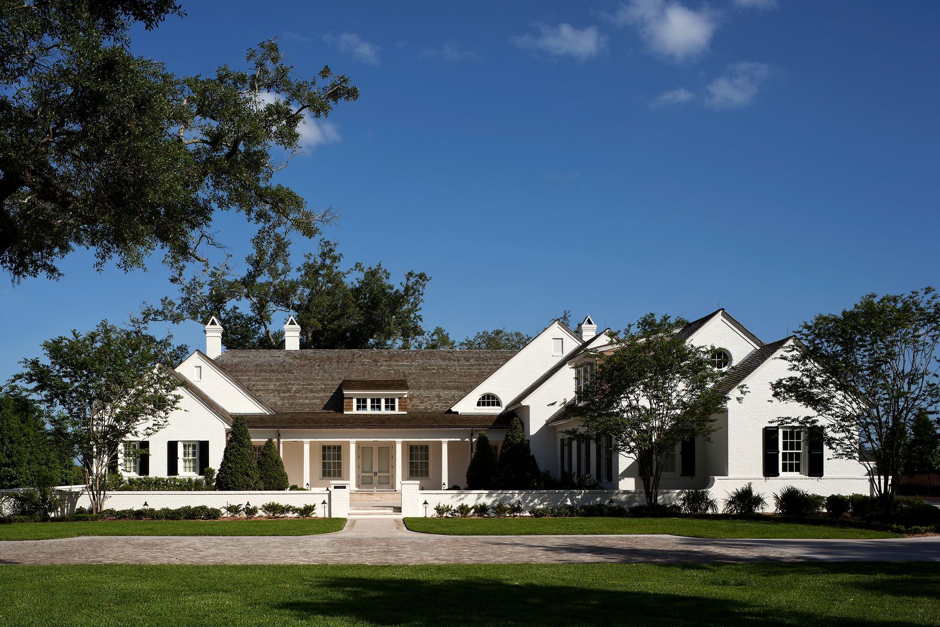 White, two-story house with a brown roof and black shutters, set against a blue sky.