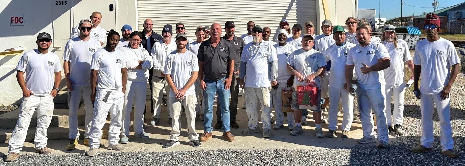 Group of people in white attire, posing outdoors in front of a building.