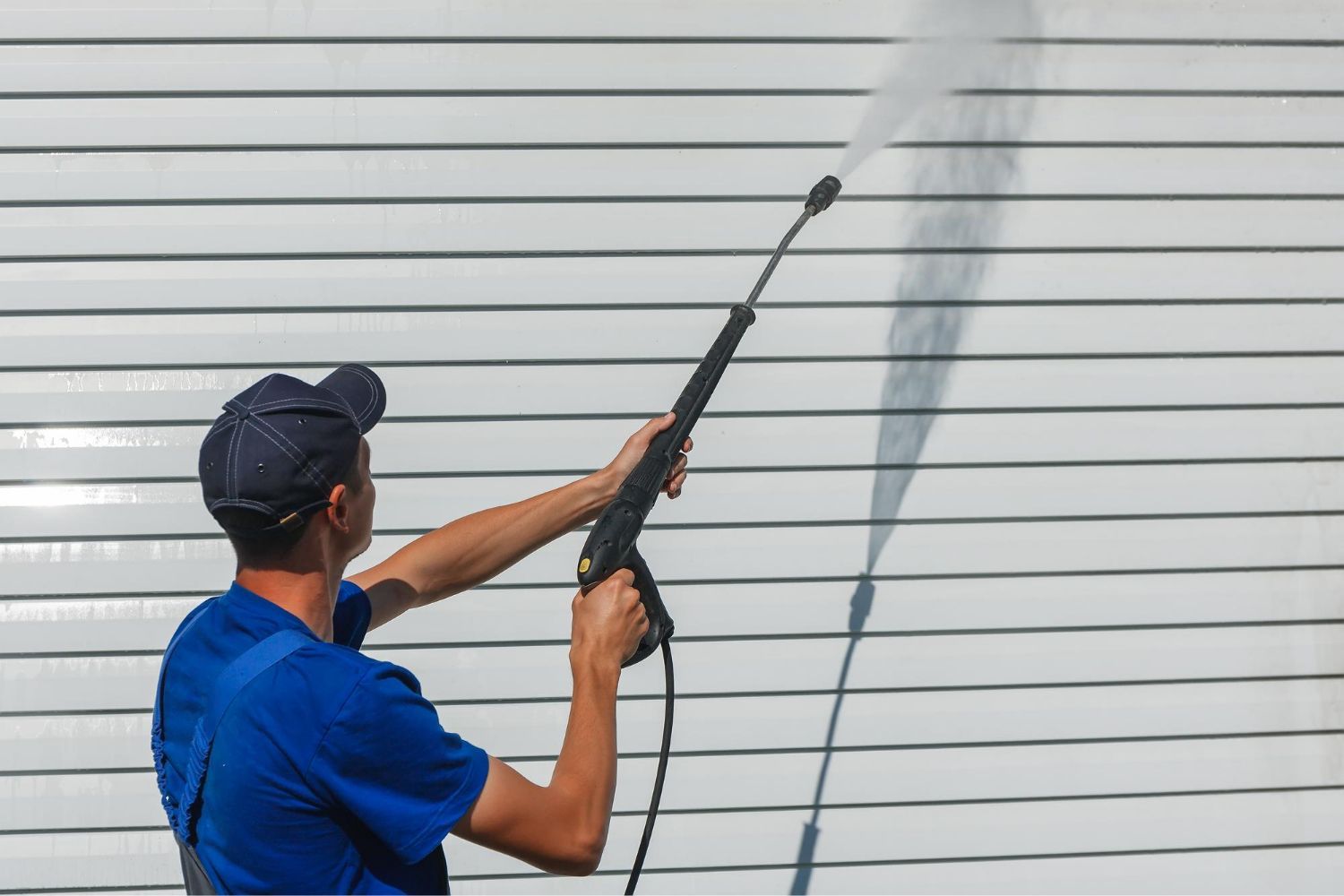 A man is using a high pressure washer to clean a garage door.