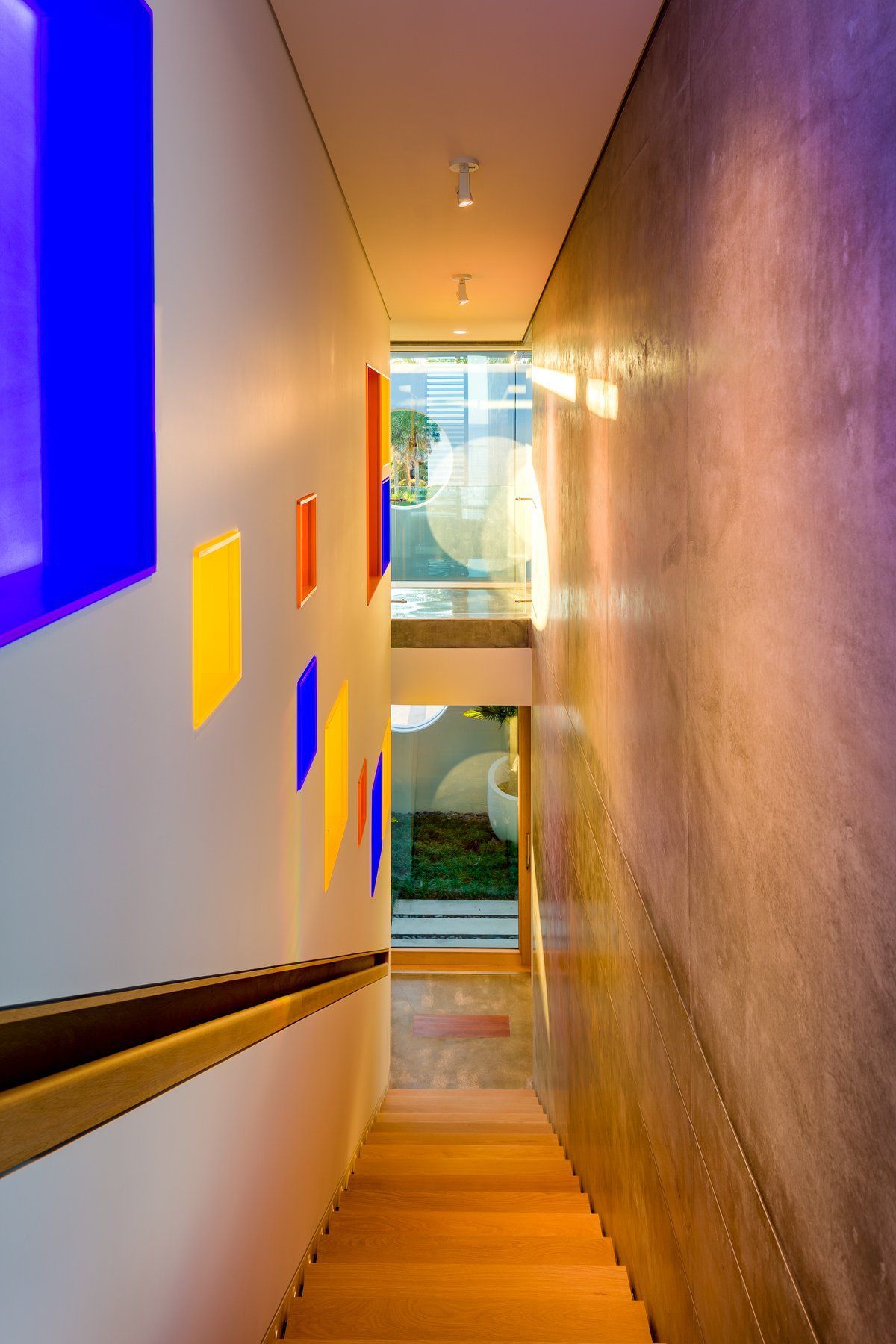 Stairwell with colorful light panels on the left and textured wall on the right, leading to a window with outdoor view.