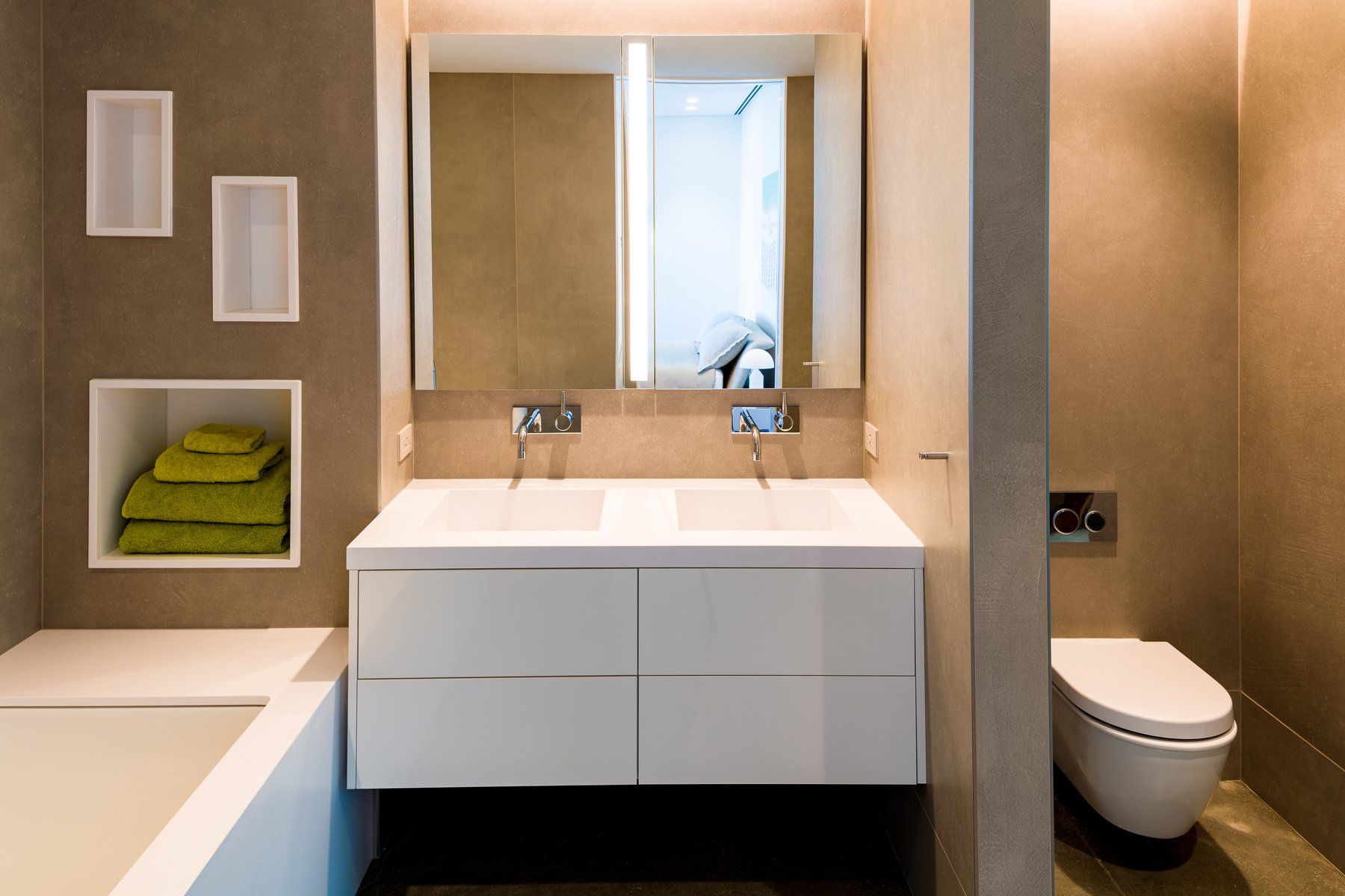 Modern bathroom with white floating vanity, large mirror, and recessed shelves with green towels.