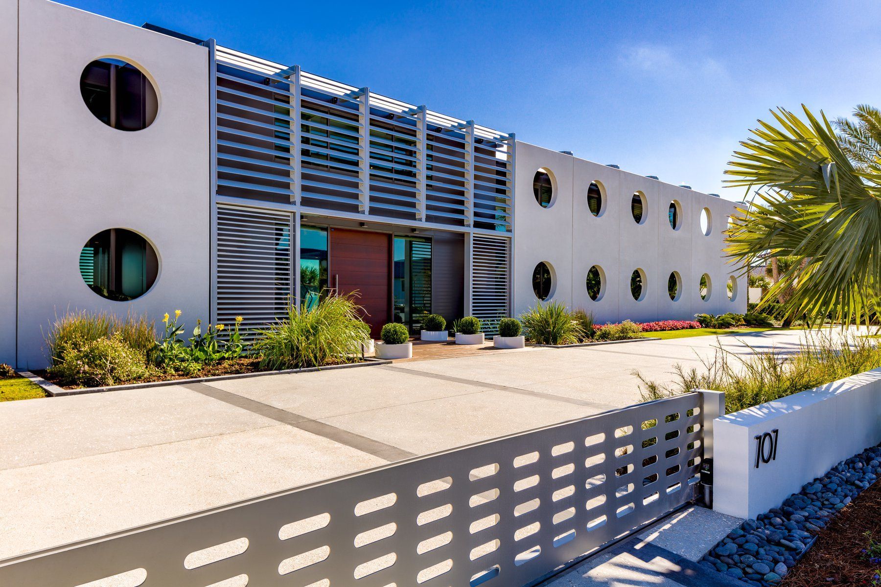 Modern white building with circular windows and a grey gate, sunny day.