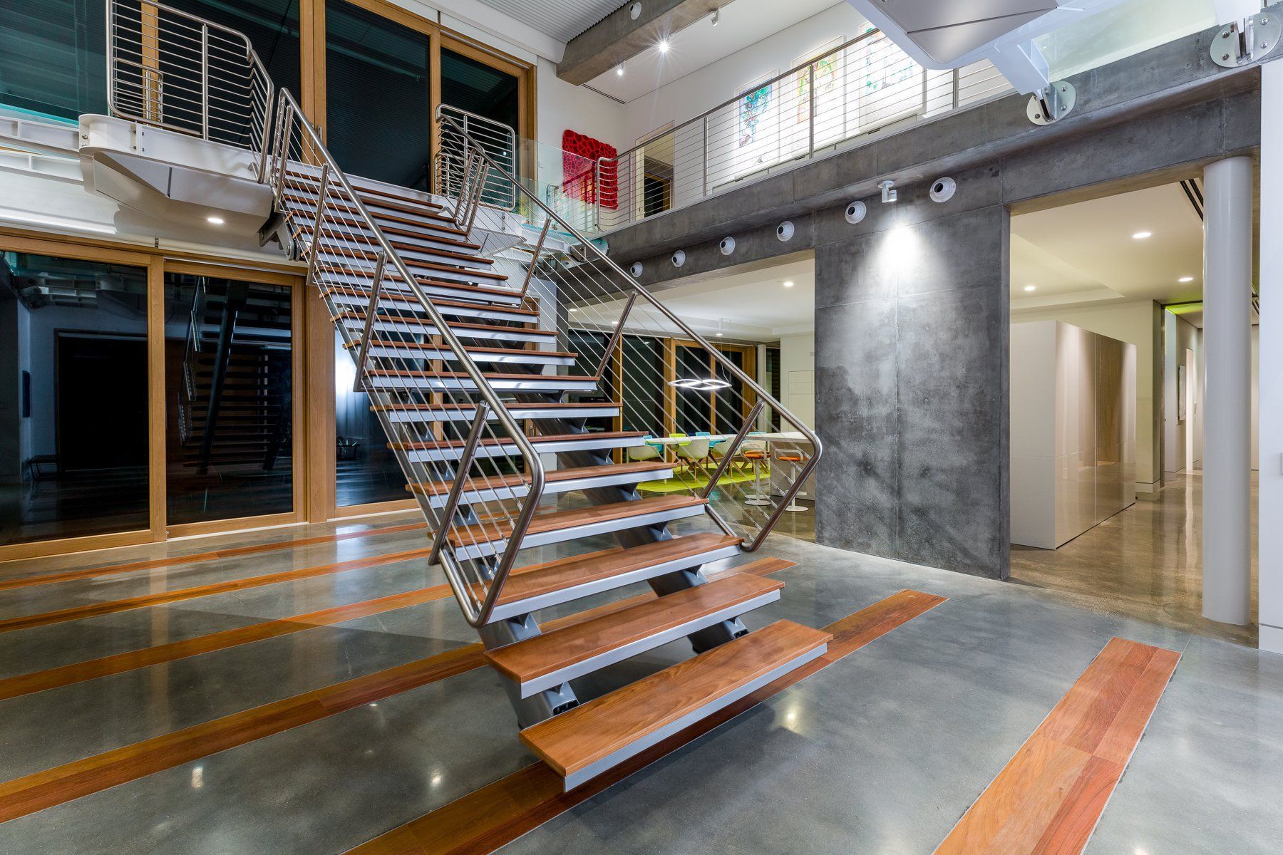 Modern interior with floating wooden staircase, concrete walls, and glass doors.