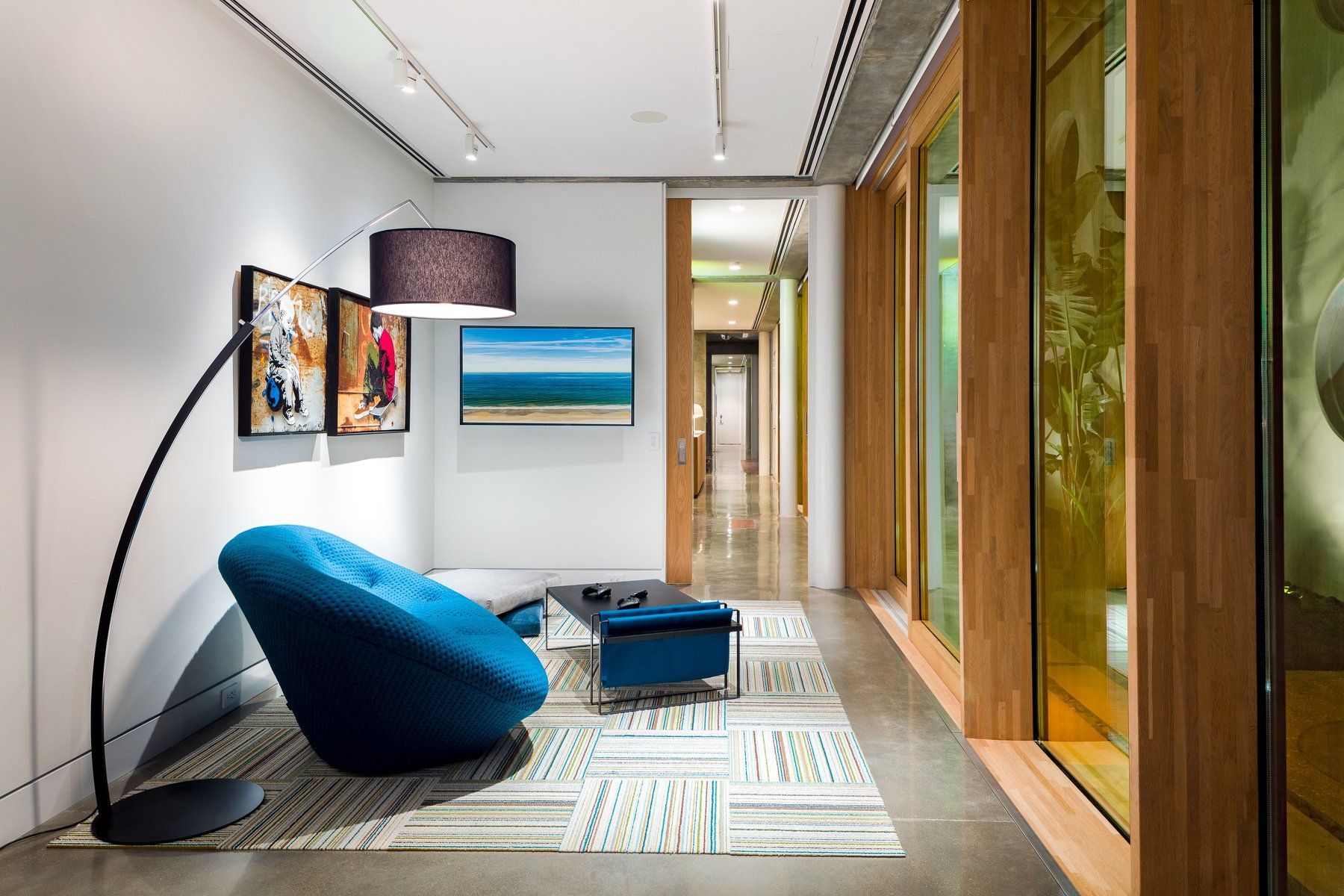 Modern hallway with blue chair, small table, rug, artwork, and wooden paneling.