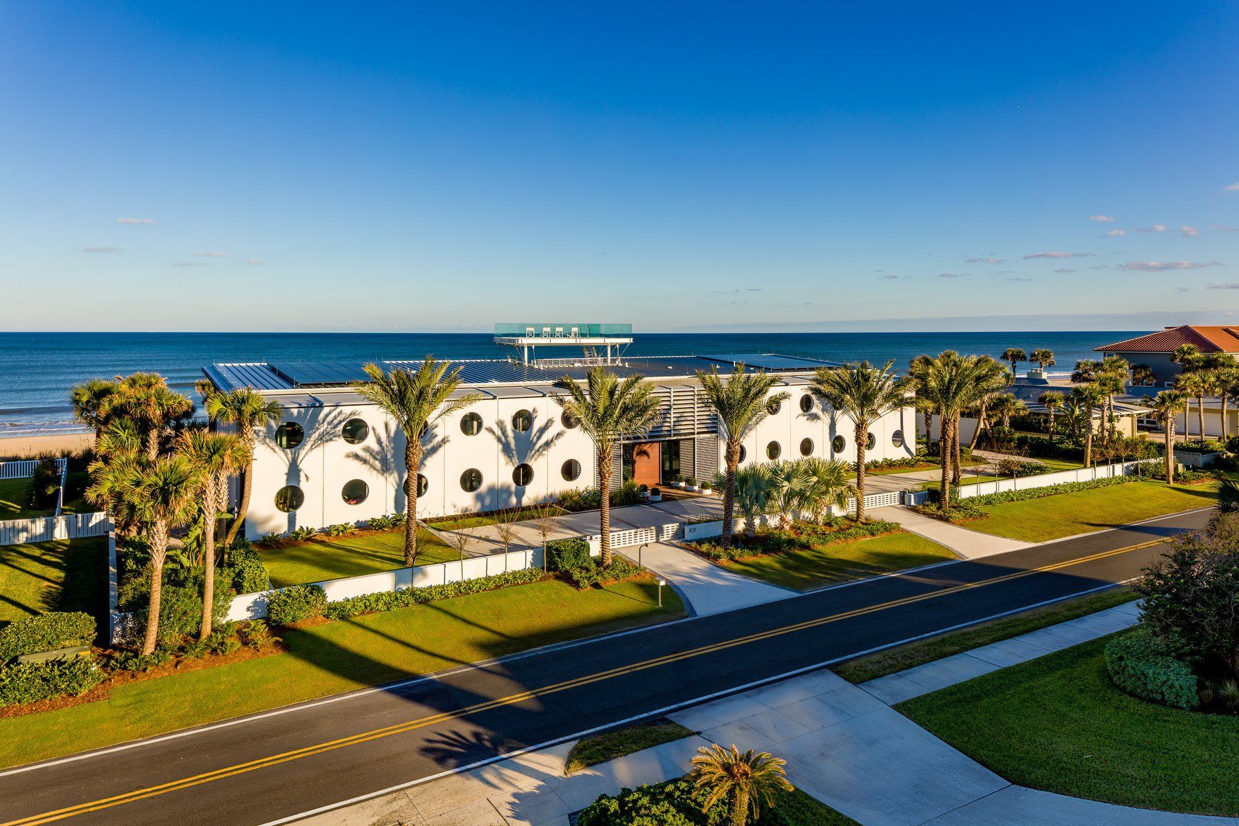 White building with porthole windows, palm trees, and beach in the background.