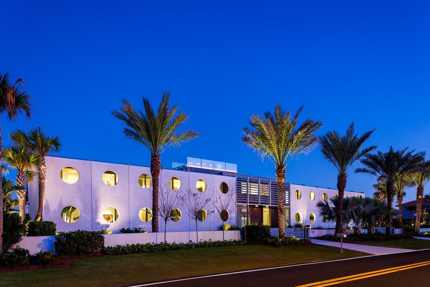White building with circular windows, palm trees, and blue twilight sky.