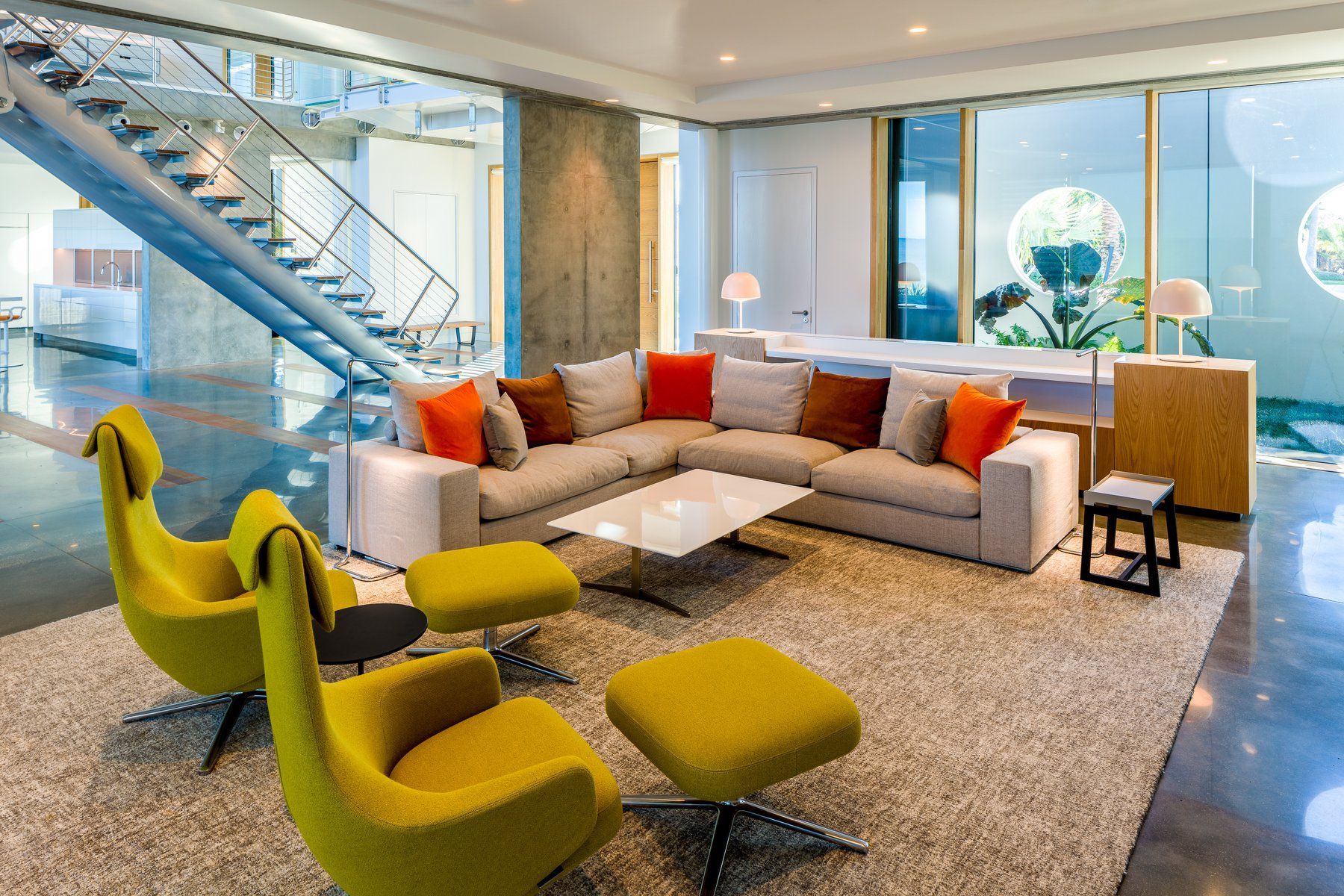 Modern living room with yellow chairs, beige sectional sofa, and a staircase.