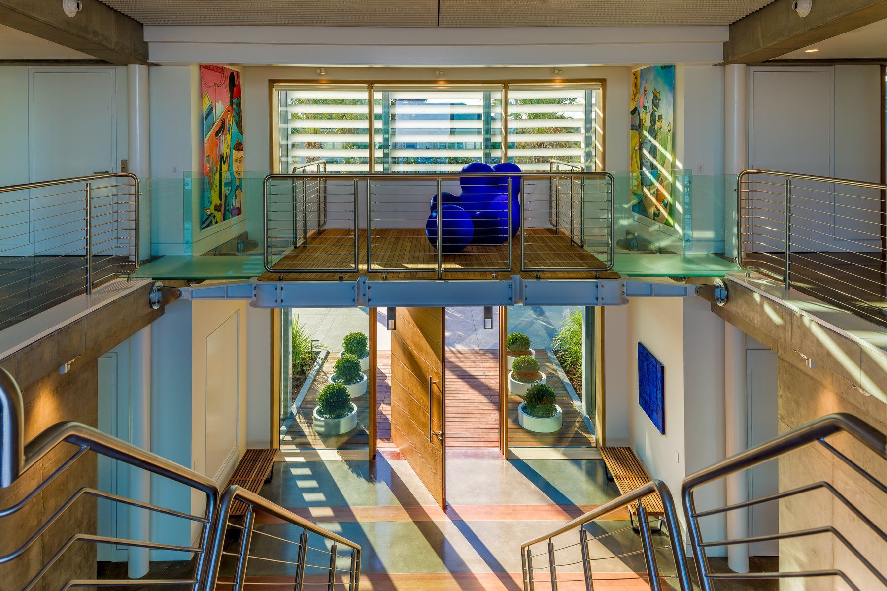 Stairwell with open doors, leading to a mezzanine with blue art, sunlight streaming through.
