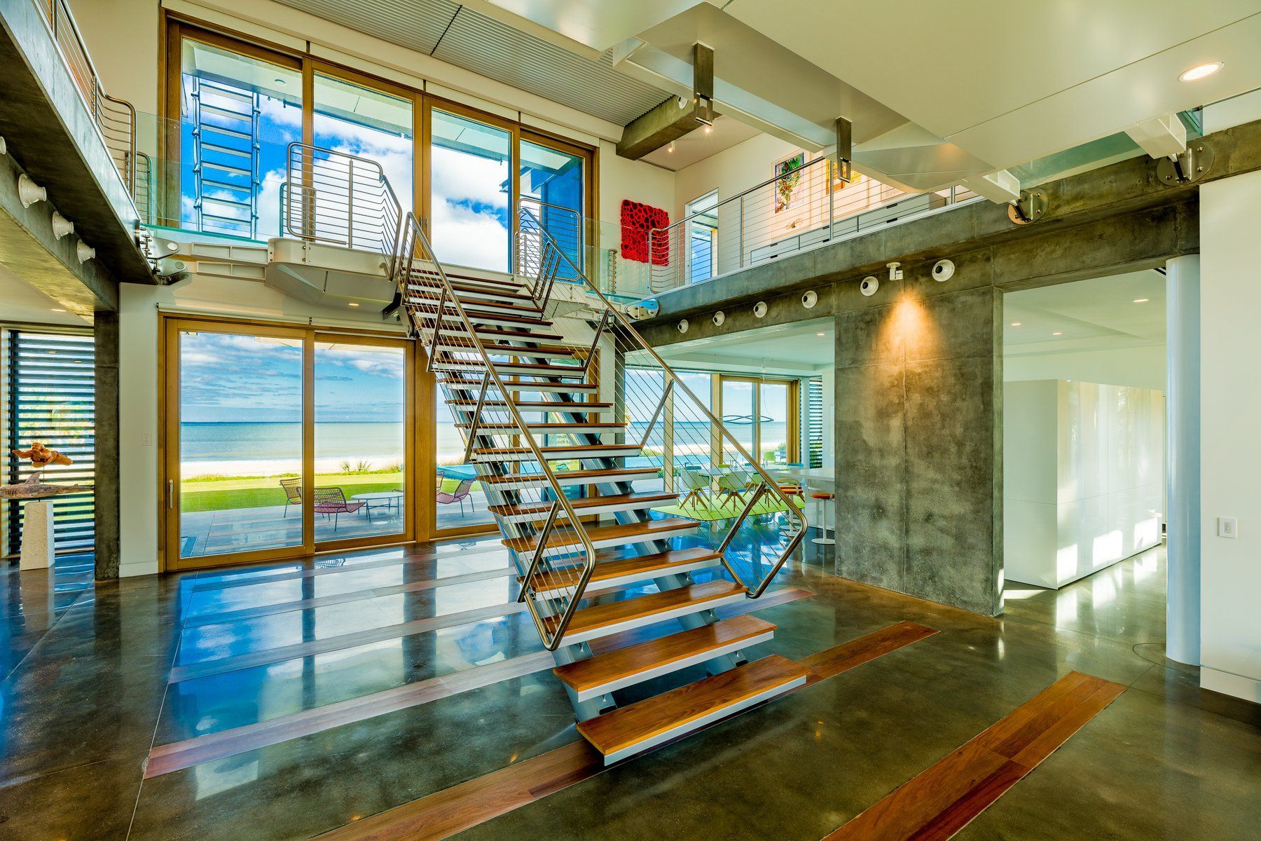 Spacious modern home interior with ocean view, metal staircase, and concrete floors.