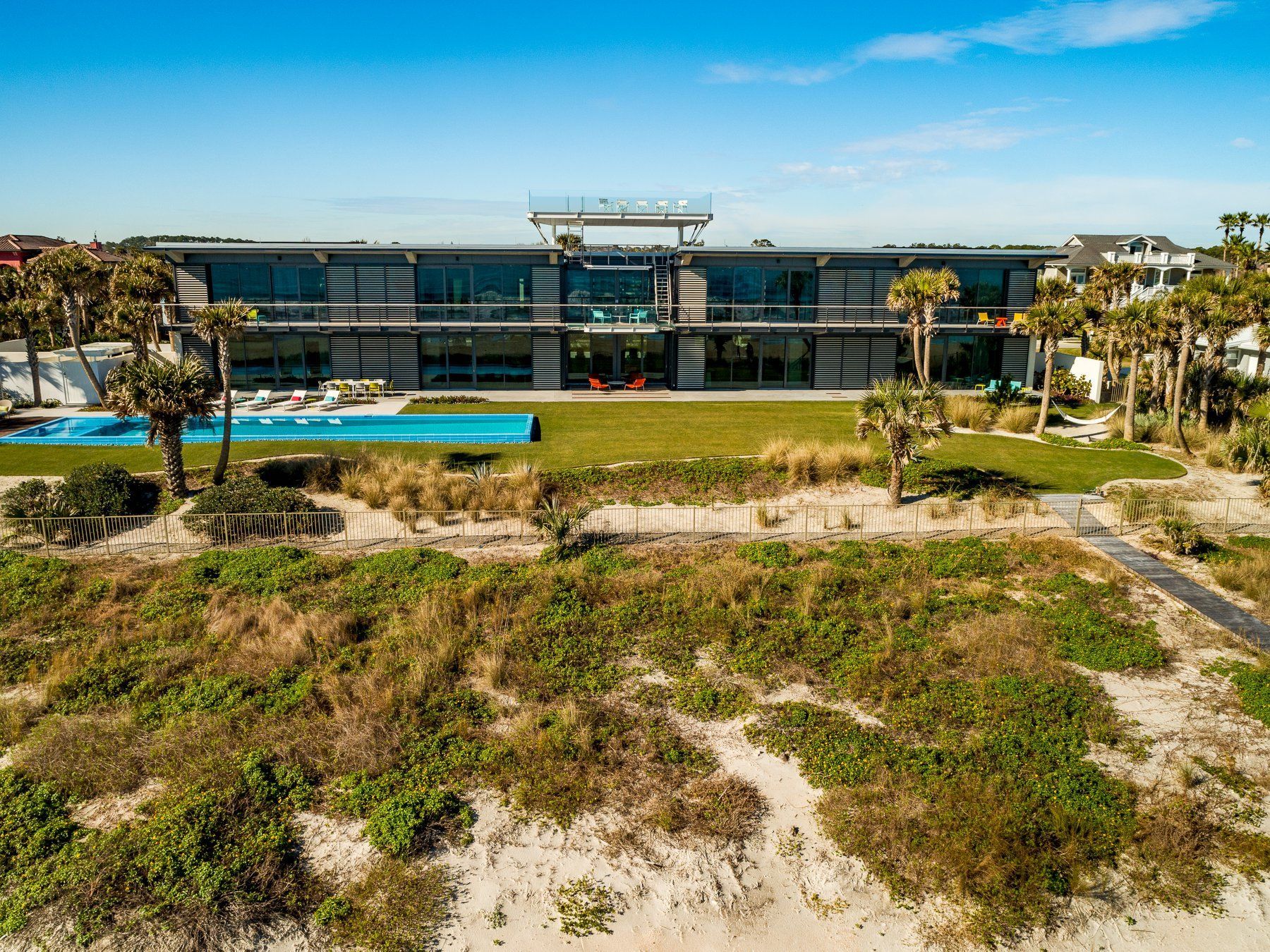 Modern beachfront house with a long turquoise pool and green lawn; sunny day.