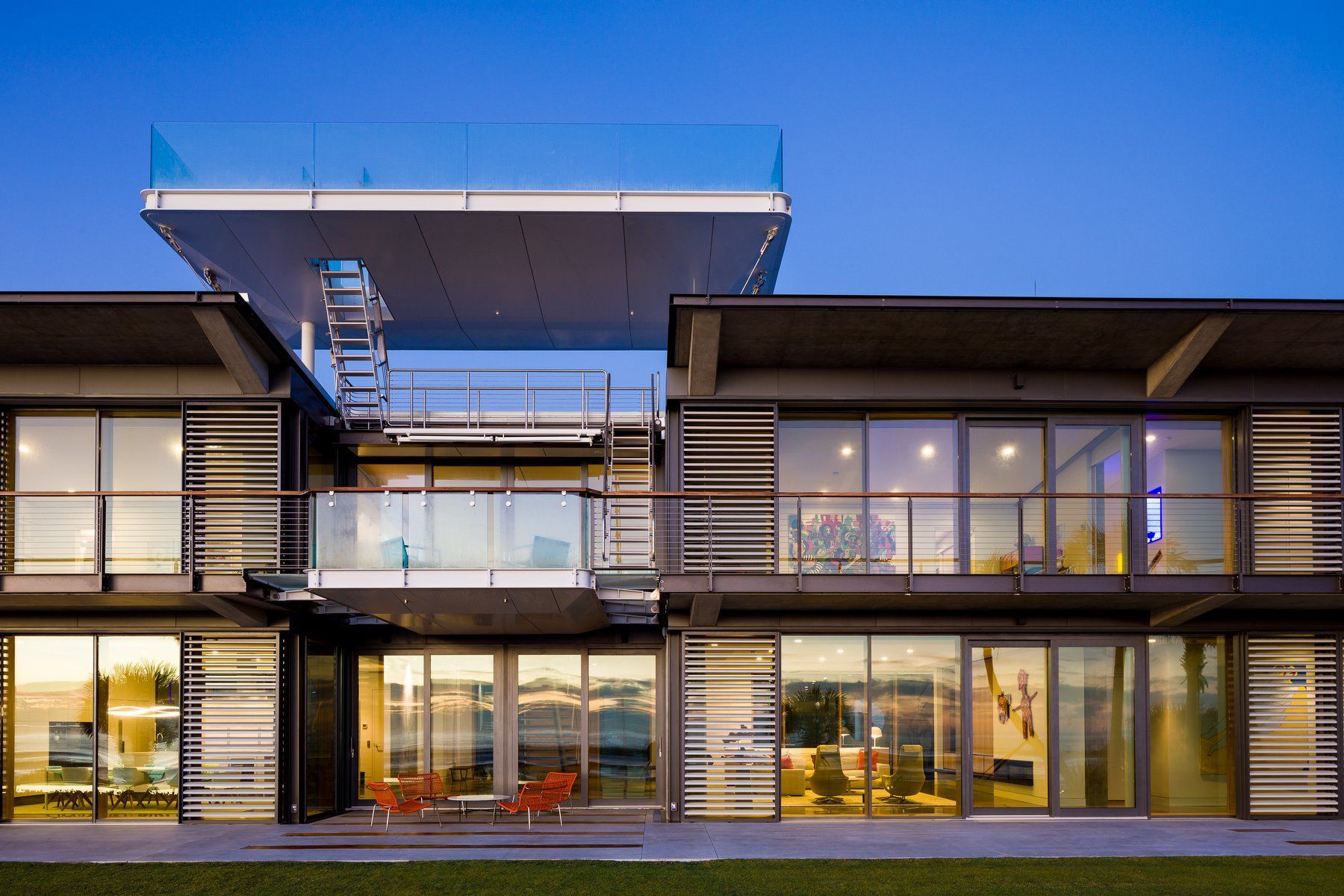 Modern multi-story home with glass walls, balconies, and a rooftop deck.