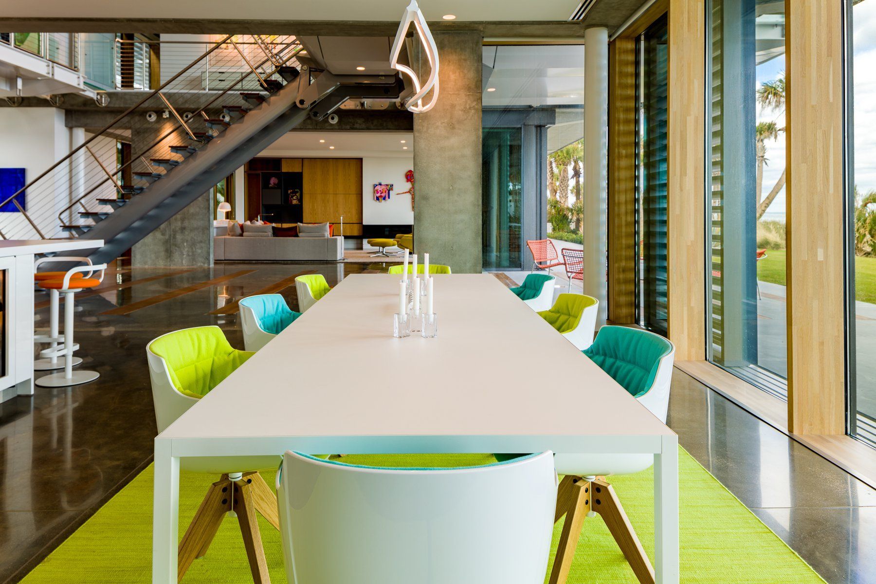 Modern dining room with long white table, colorful chairs, and large windows.