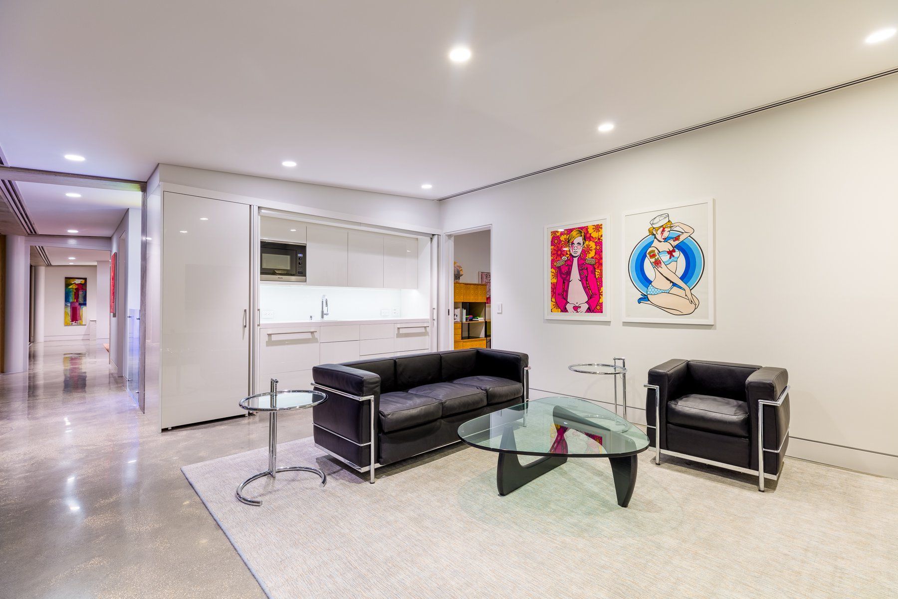 Modern living room with black furniture, art, and a hidden kitchen.