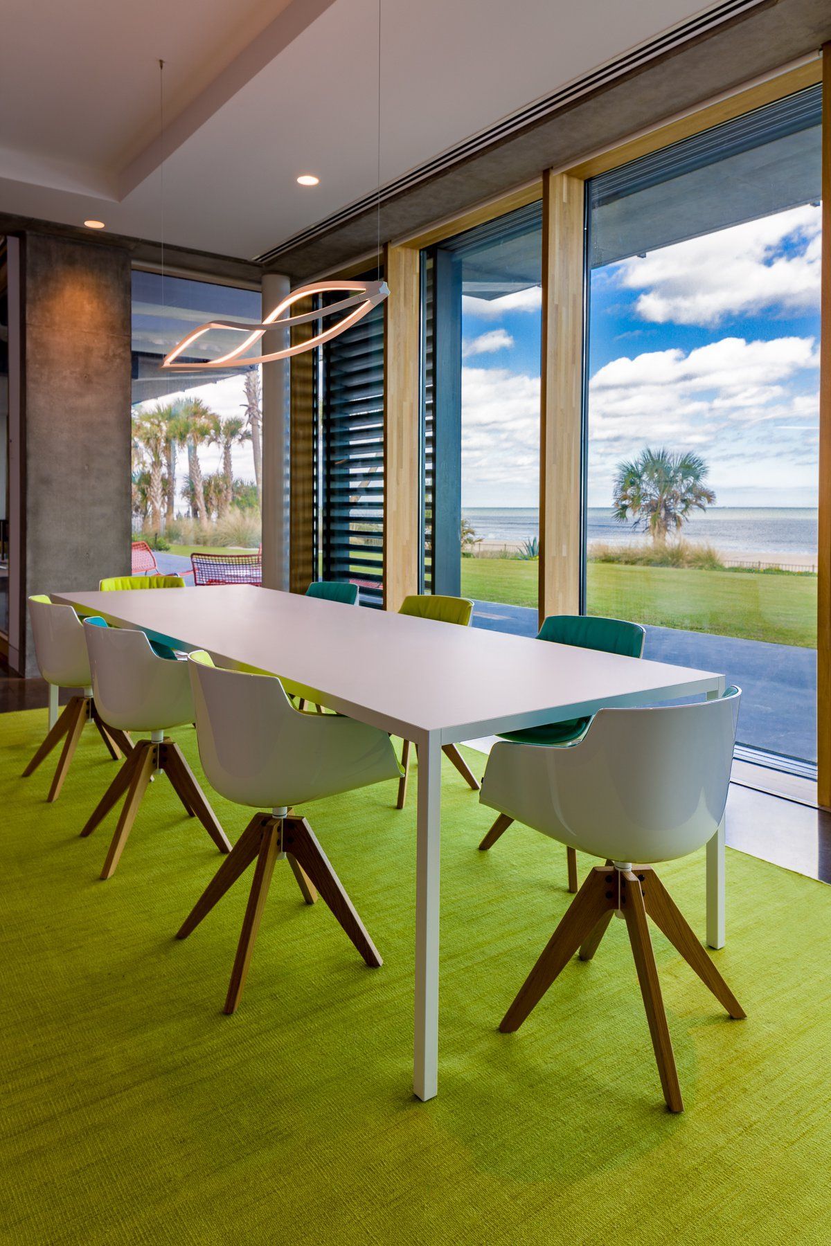 Meeting room with white table, modern chairs, green carpet, and large window overlooking the water.