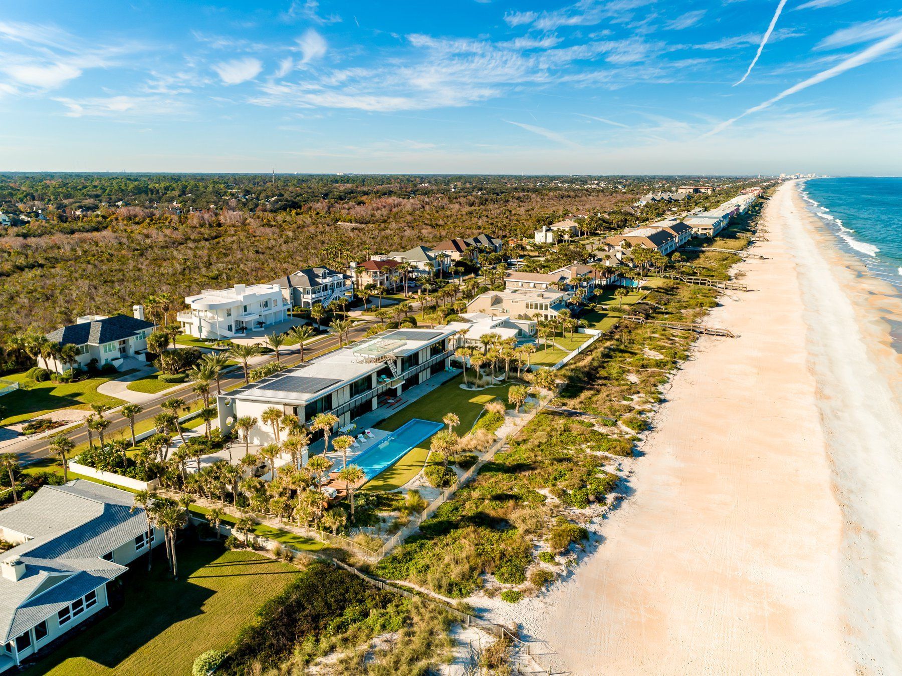 Aerial view of beachfront homes, sand, and ocean under a blue sky.