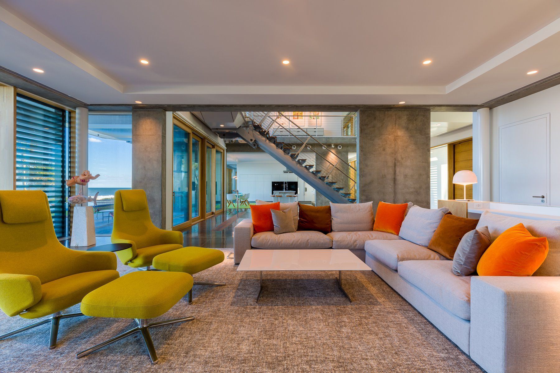 Modern living room with gray sectional sofa, yellow armchairs, and ocean view.