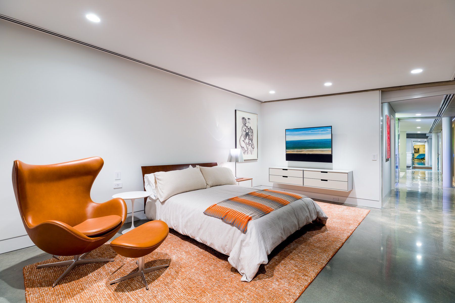 Bedroom with orange chair, bed, and neutral-toned rug, with a modern aesthetic.