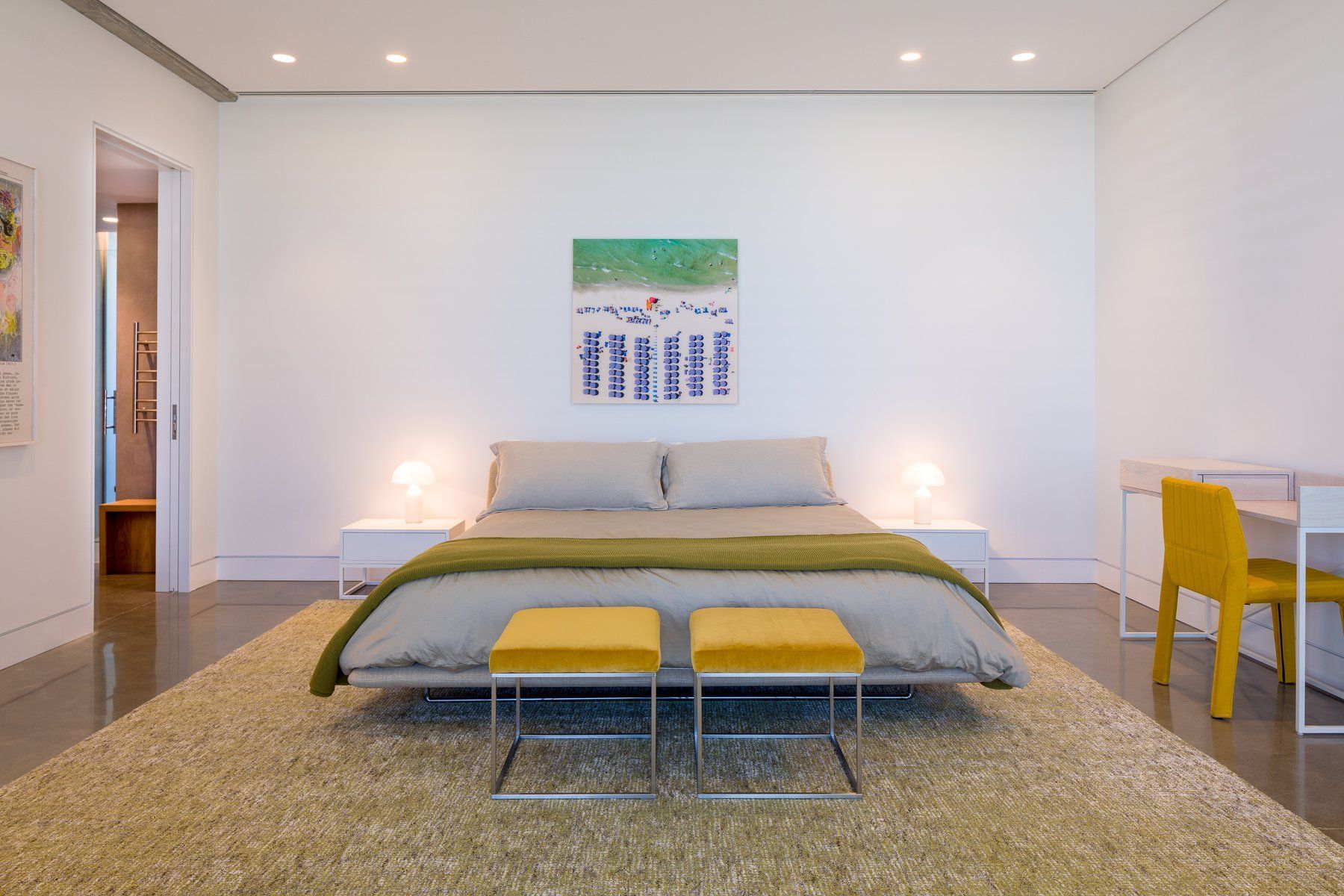 Modern bedroom: white walls, bed with gray bedding, yellow stools, and art.