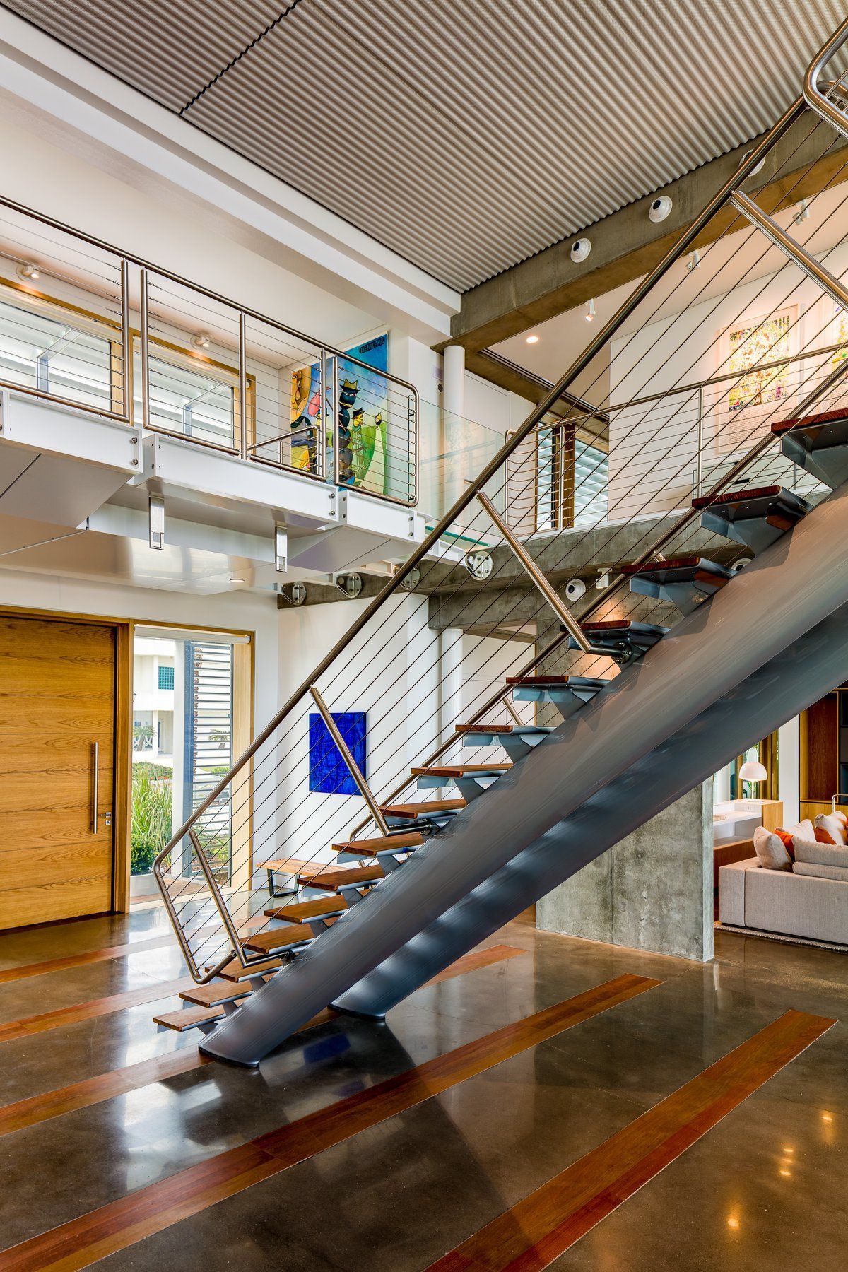 Modern interior with a metal and wooden staircase, open-plan design, high ceilings, and art.
