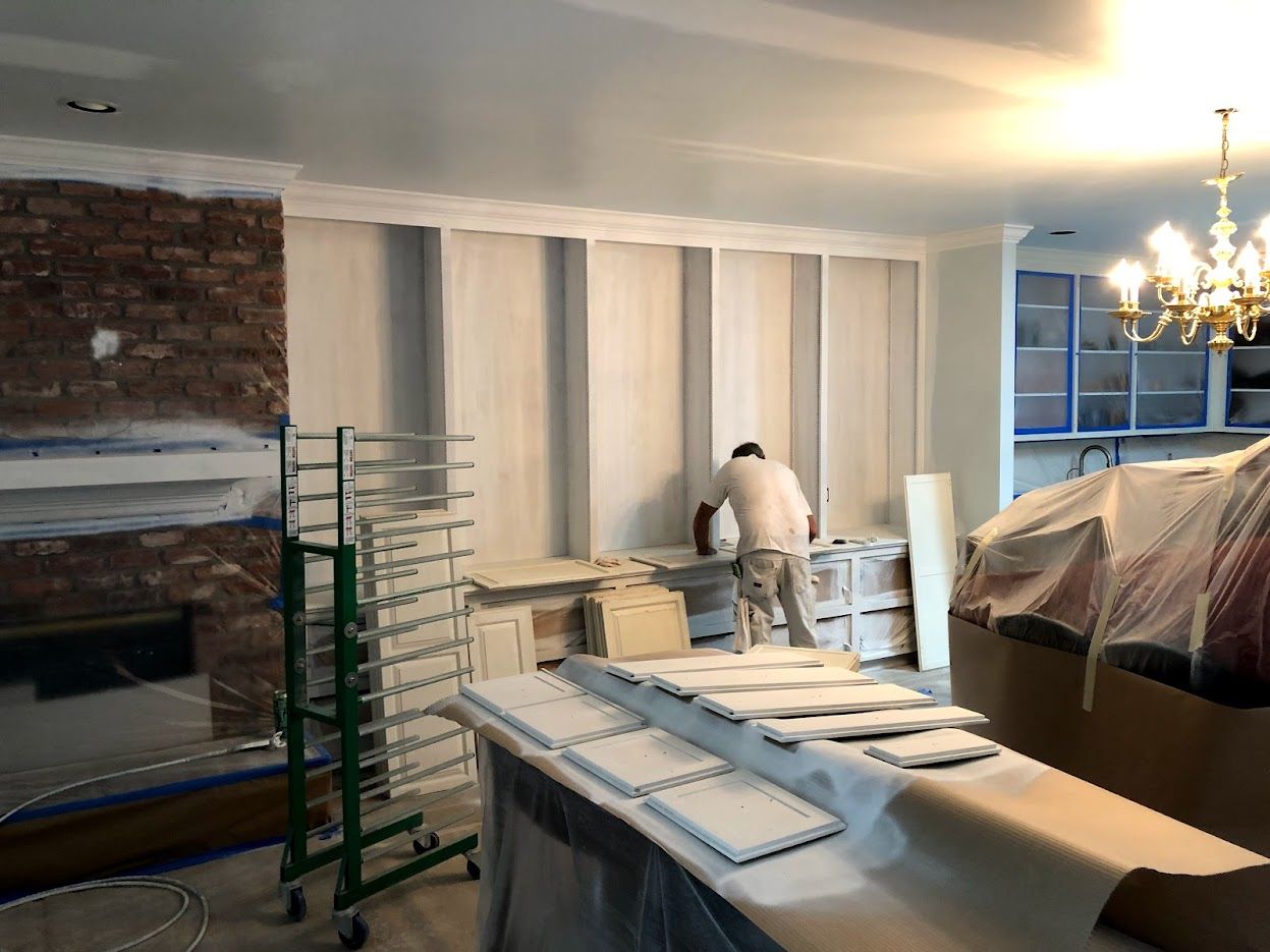 A person paints a room. Cabinets, panels, and a fireplace are being painted white.