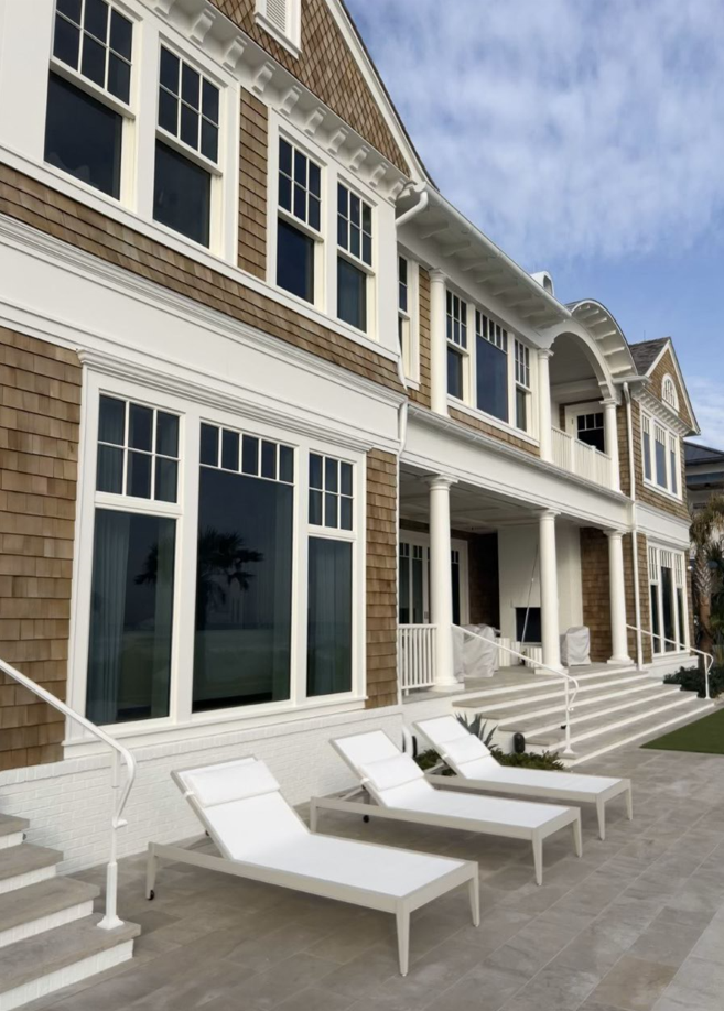 A large house with a lot of windows and lounge chairs in front of it