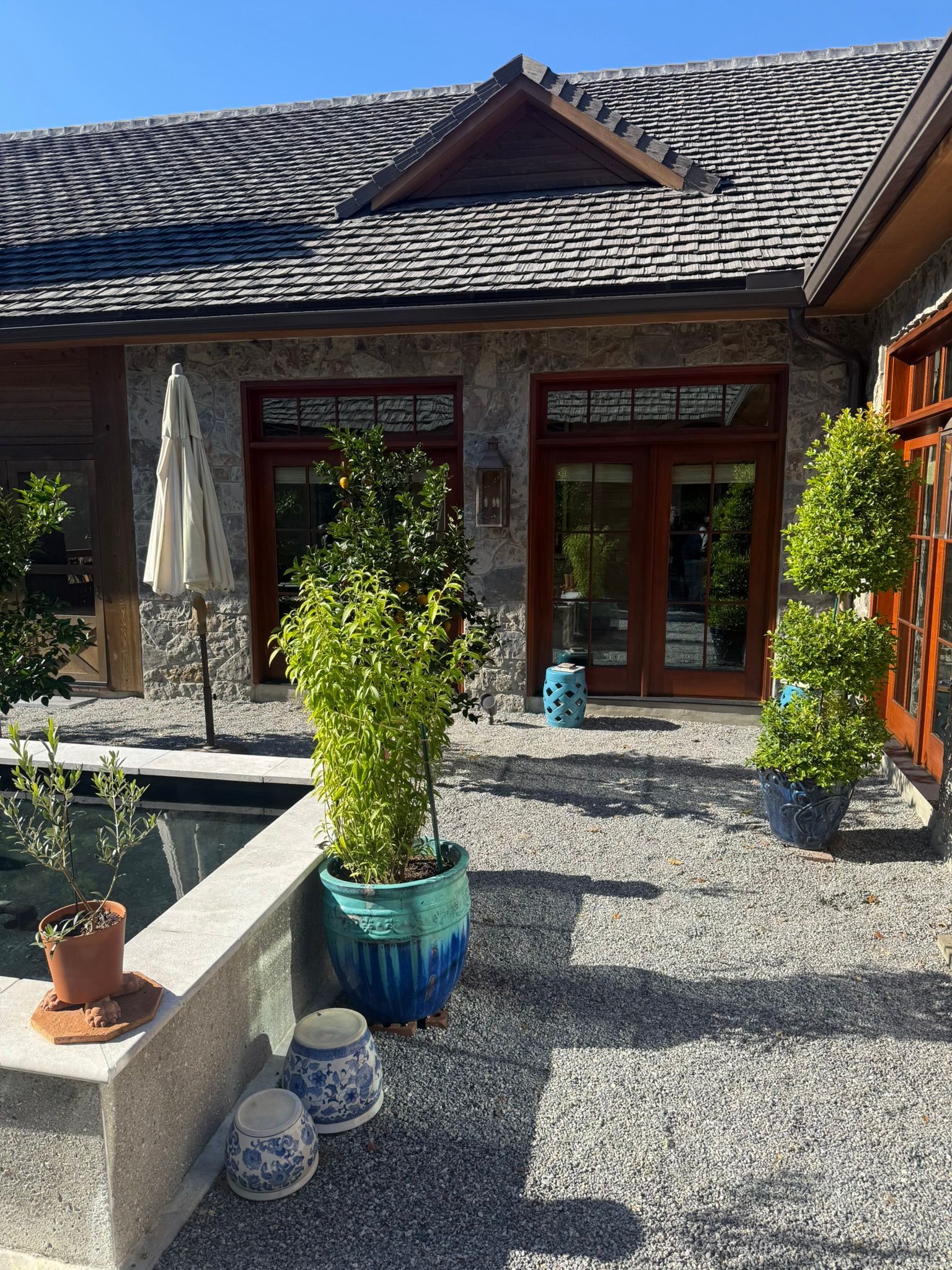 Courtyard with a stone house, dark tiled roof, potted plants, and a small water feature in front