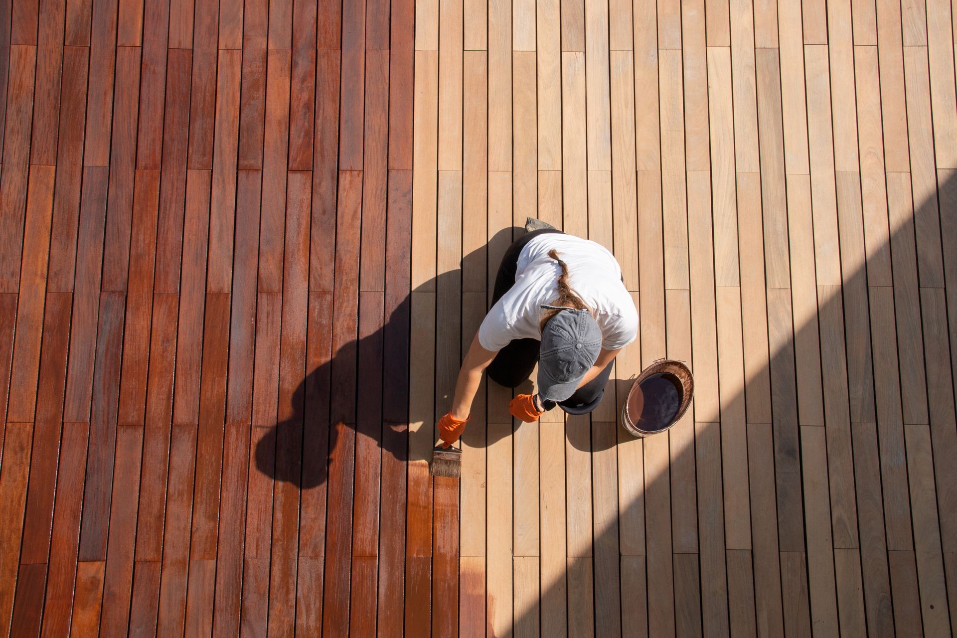 Person staining a wooden deck; half is stained dark brown, the other half is natural.