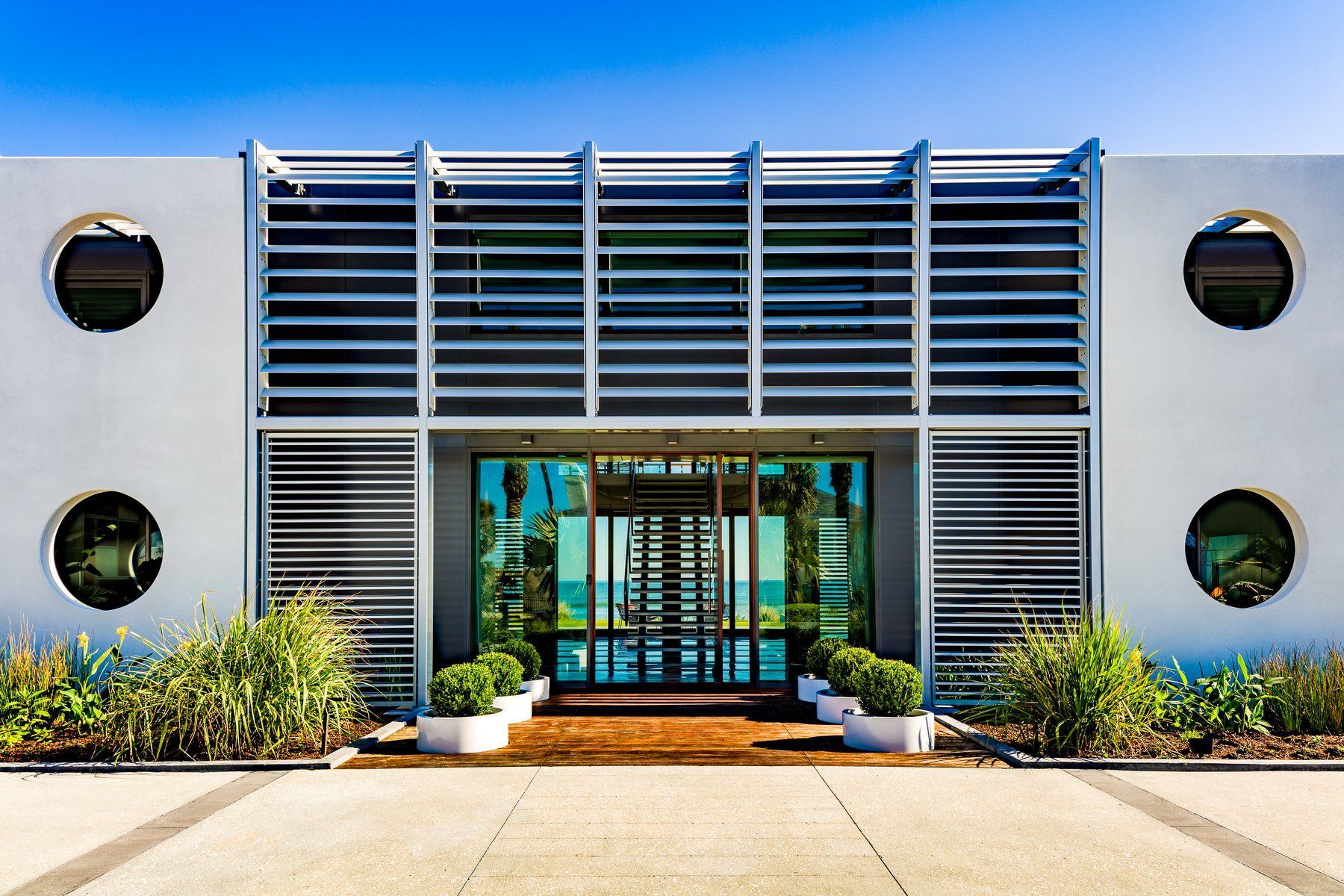 Modern white building with horizontal louvers, glass doors, and circular windows.