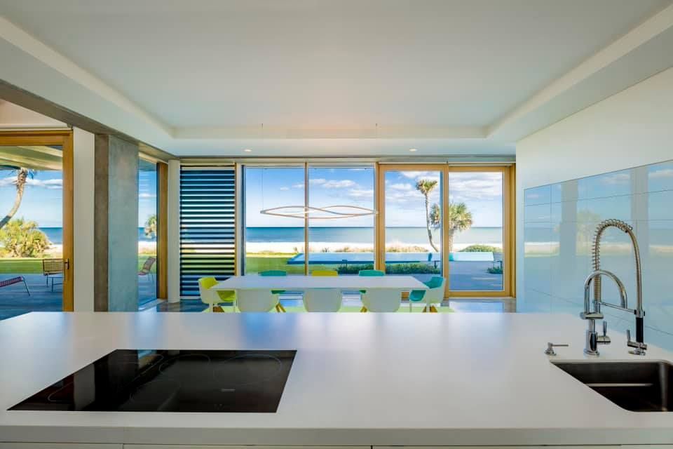 Modern kitchen with white countertop, sink, and cooktop, overlooking a beach and ocean view.